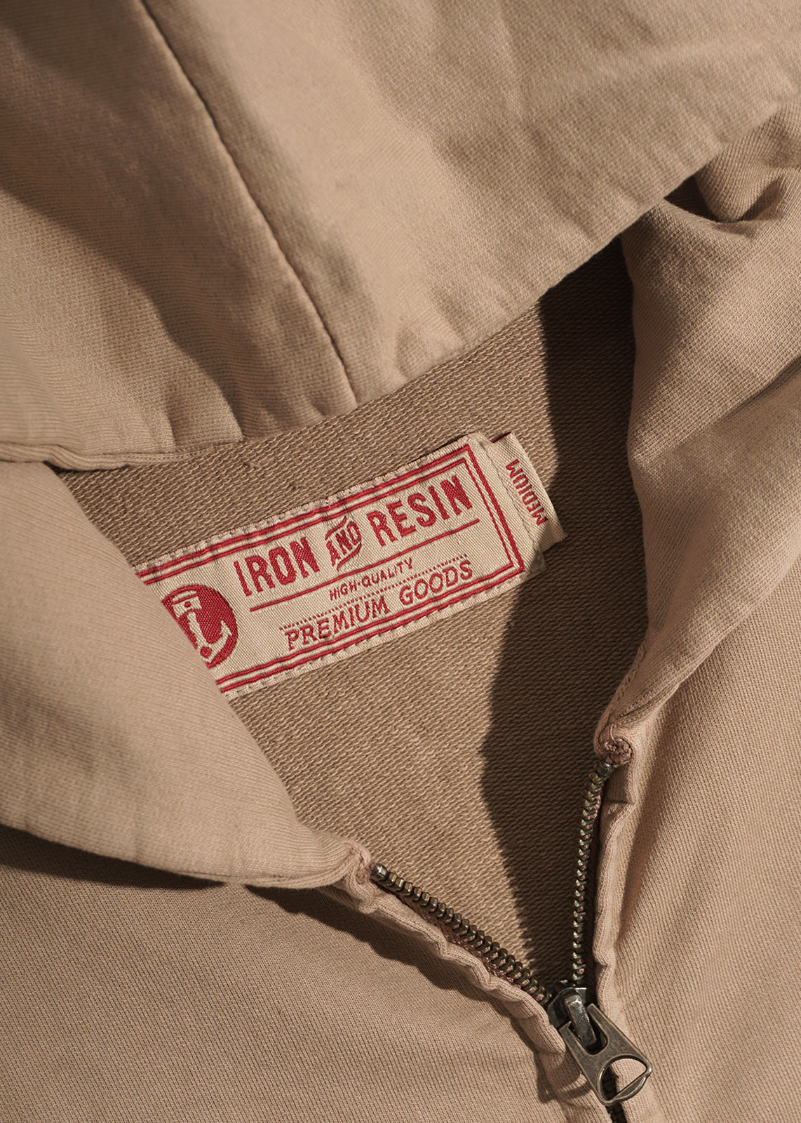 Close-up of a beige jacket with a visible Iron and Resin label, highlighting the zipper and fabric texture.