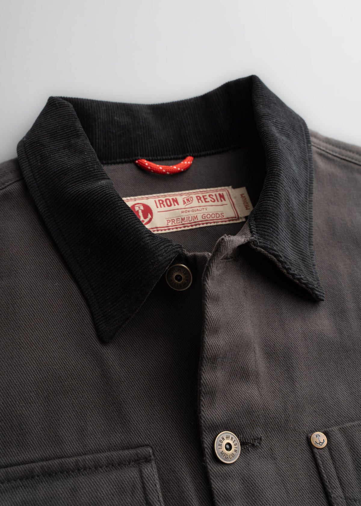 Close-up of a dark jacket with a corduroy collar, featuring Iron and Resin label and buttons, highlighting premium craftsmanship.