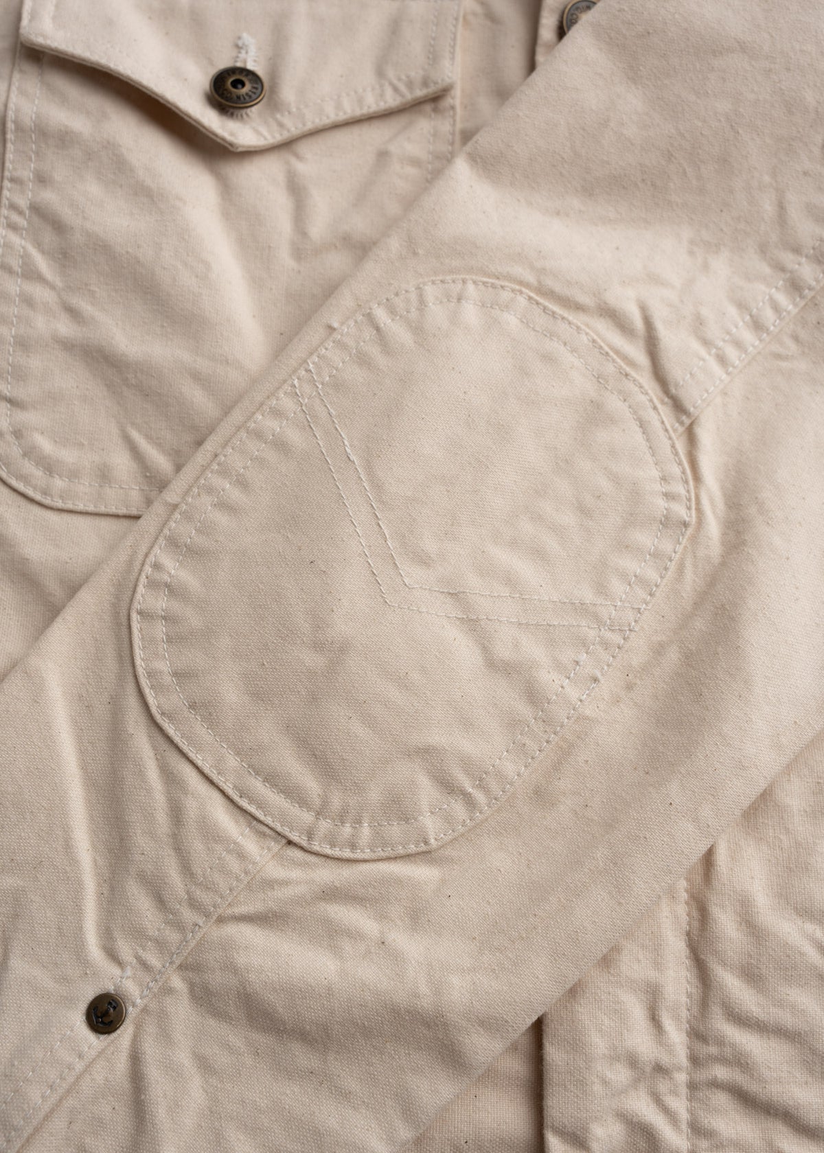 Men’s cotton canvas jacket with boxy fit, workwear outerwear with classic utility design, details in stitching, close-up shot to showcase elbow pads and custom buttons