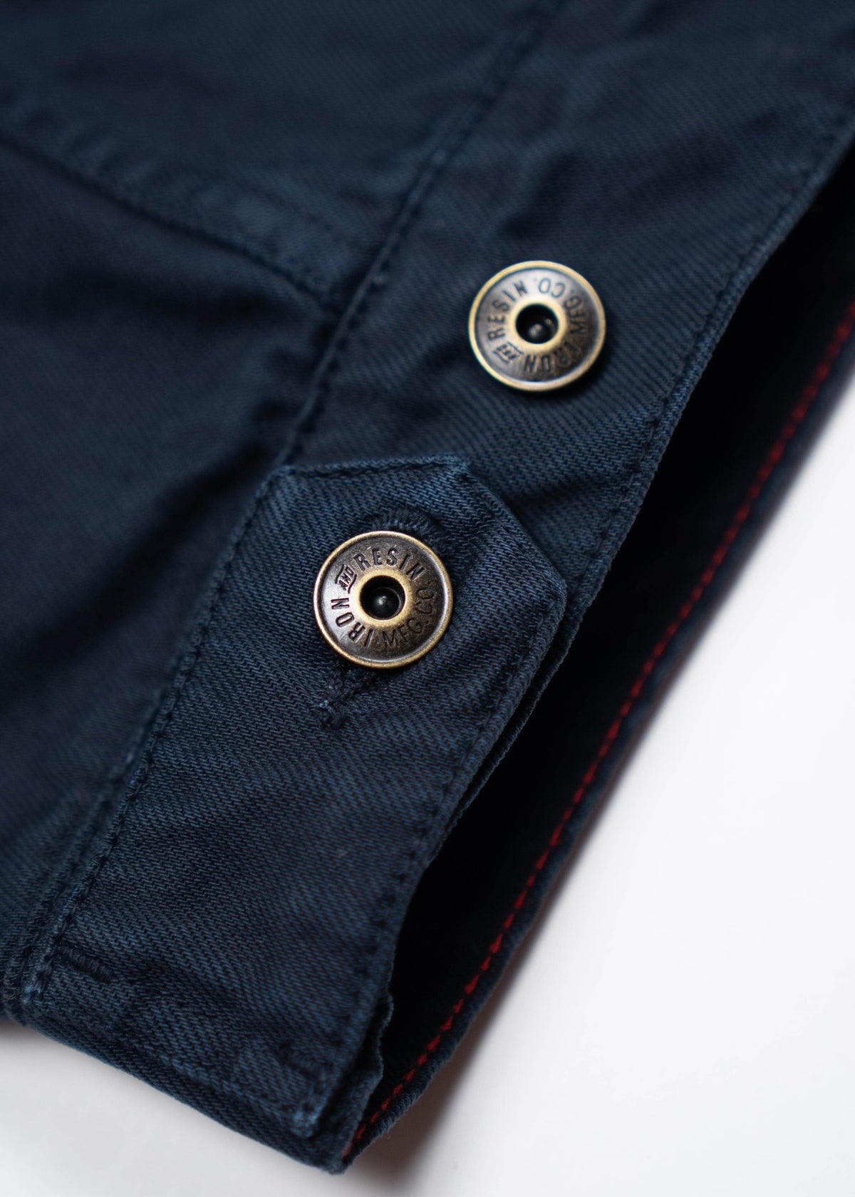 Close-up of a navy blue fabric with two metallic buttons, showing detailed stitching and texture on a white background.