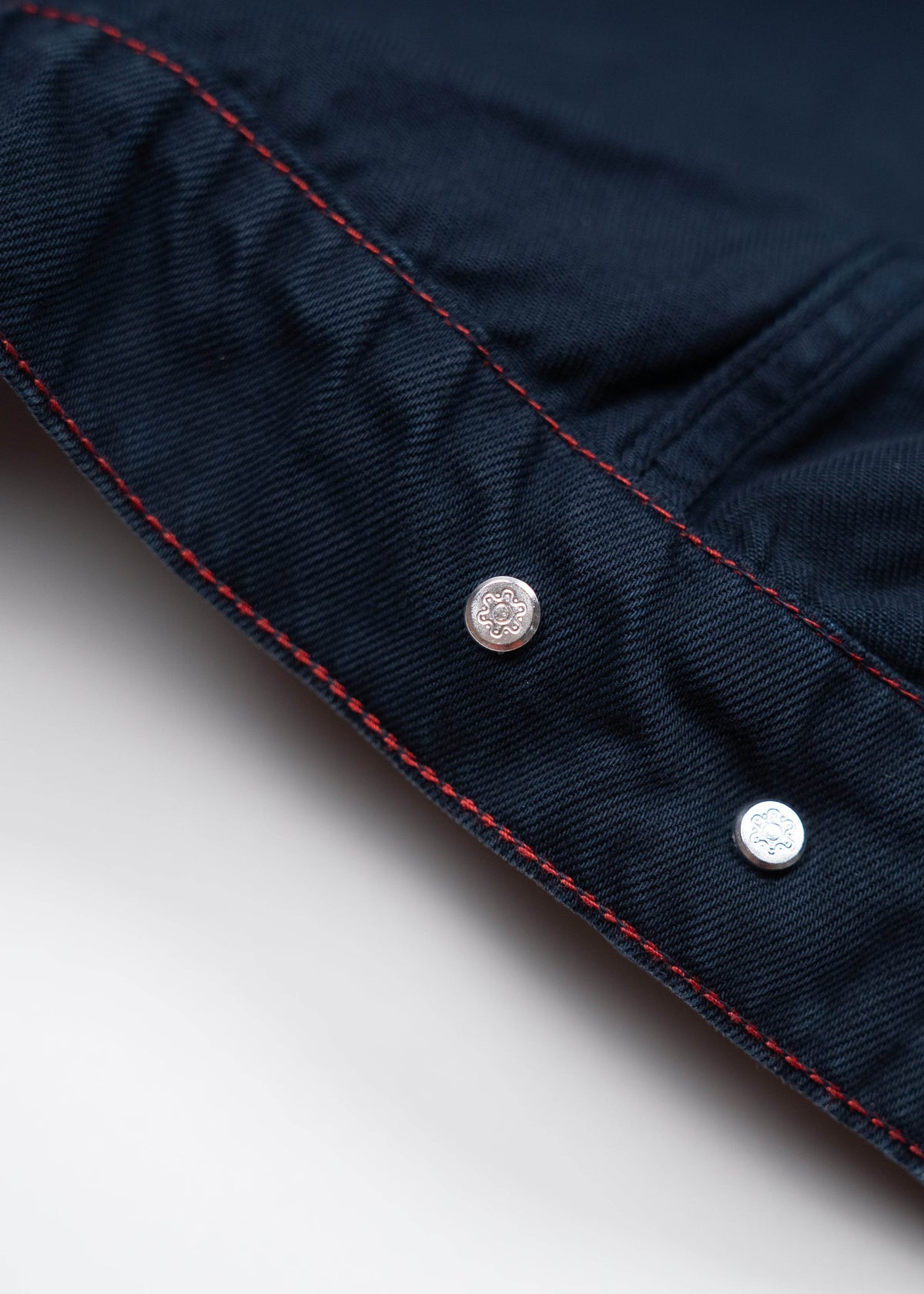 Close-up of a navy fabric with red stitching and two silver buttons, showcasing detailed craftsmanship and design elements.