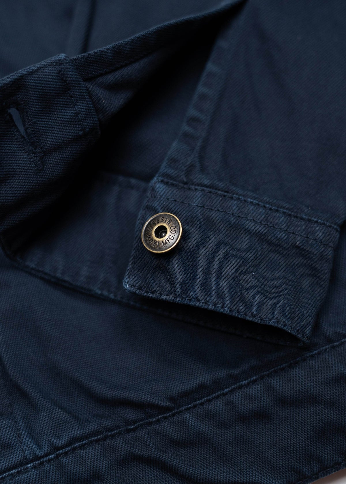 Close-up of a navy blue fabric with a metal button. The button is engraved, adding a touch of detail to the garment.