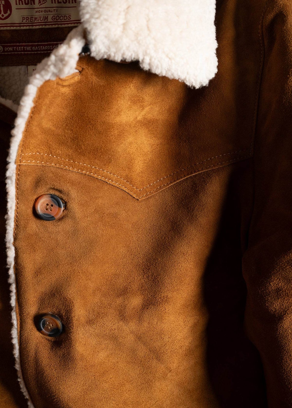 Close-up of a brown suede jacket with white shearling collar and buttons, highlighting texture and craftsmanship.
