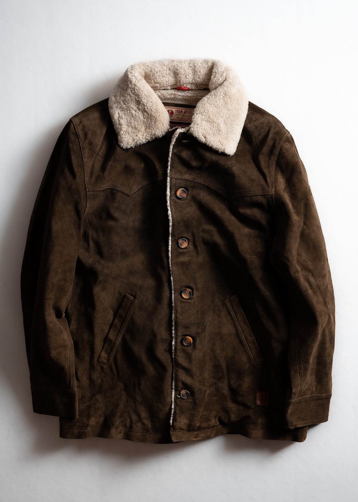 Brown suede jacket with a warm, fluffy shearling collar, buttoned front, and side pockets, laid flat on a white surface.