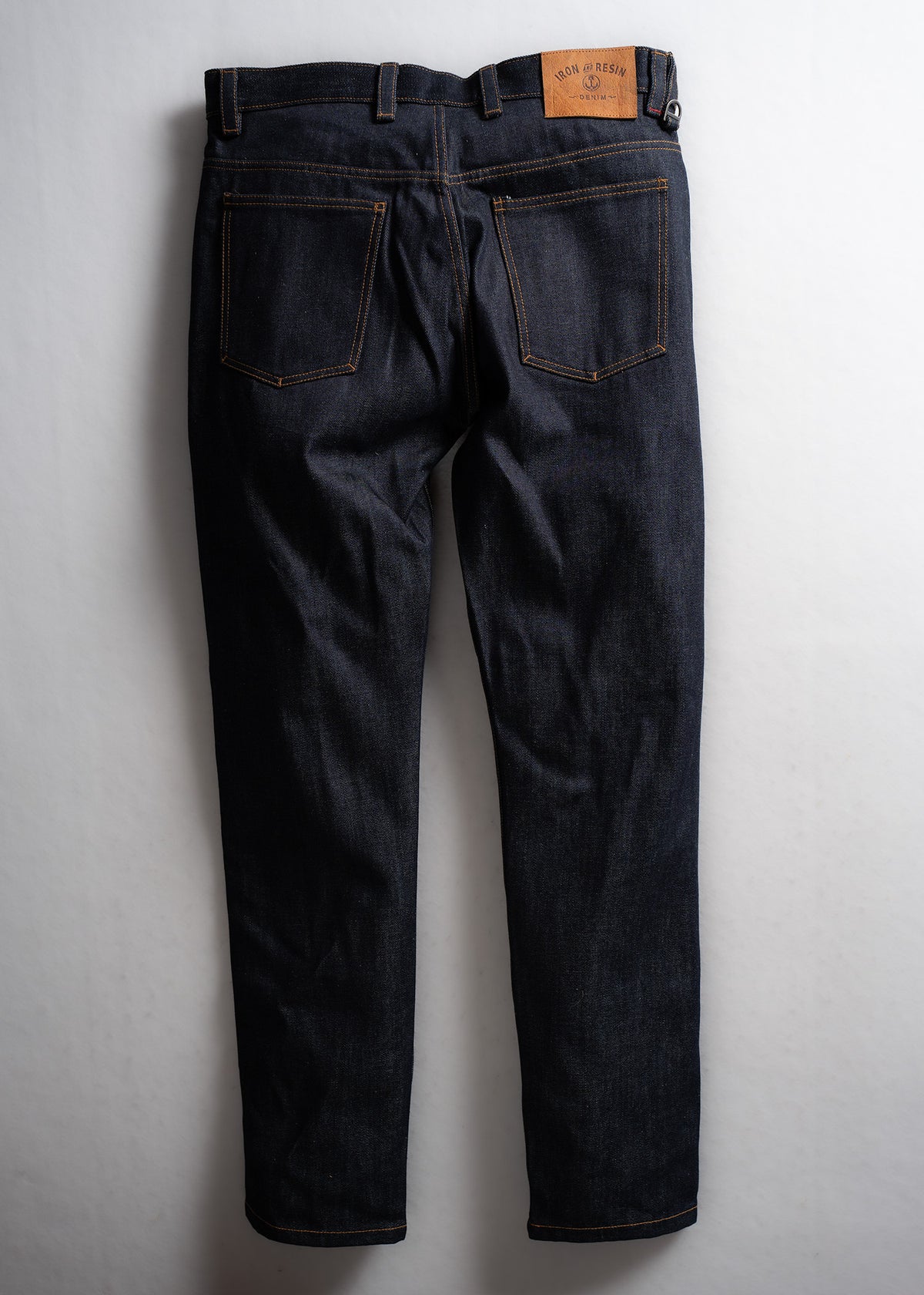 Dark denim jeans with brown stitching and a leather patch on the back, displayed against a light background.