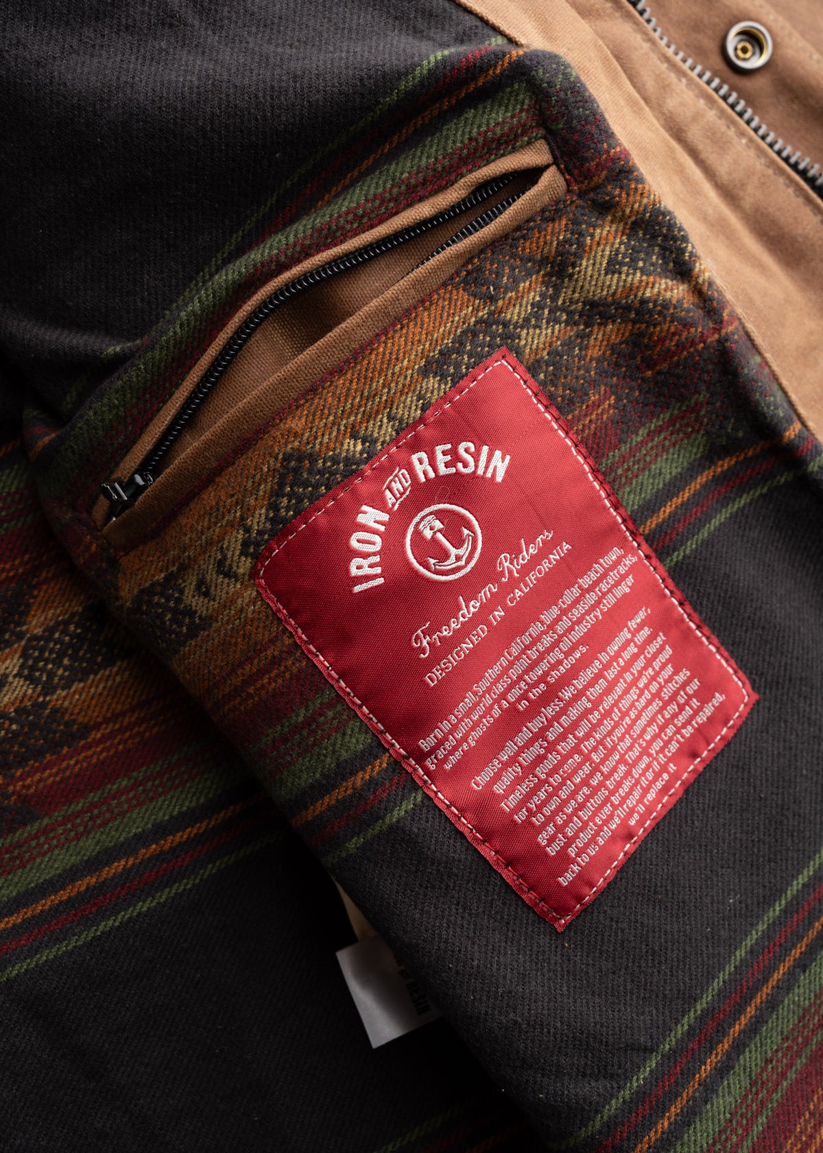 Close-up of a jacket lining with a red Iron and Resin label, featuring a zip pocket and colorful plaid fabric design.