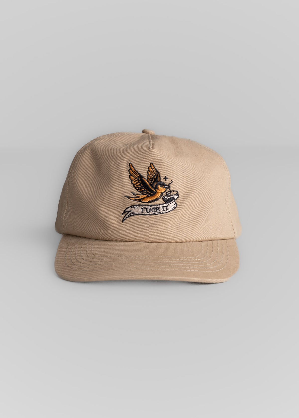 Beige cap with embroidered bird and "F*** It" text on front, set against a plain background. Casual and bold design.