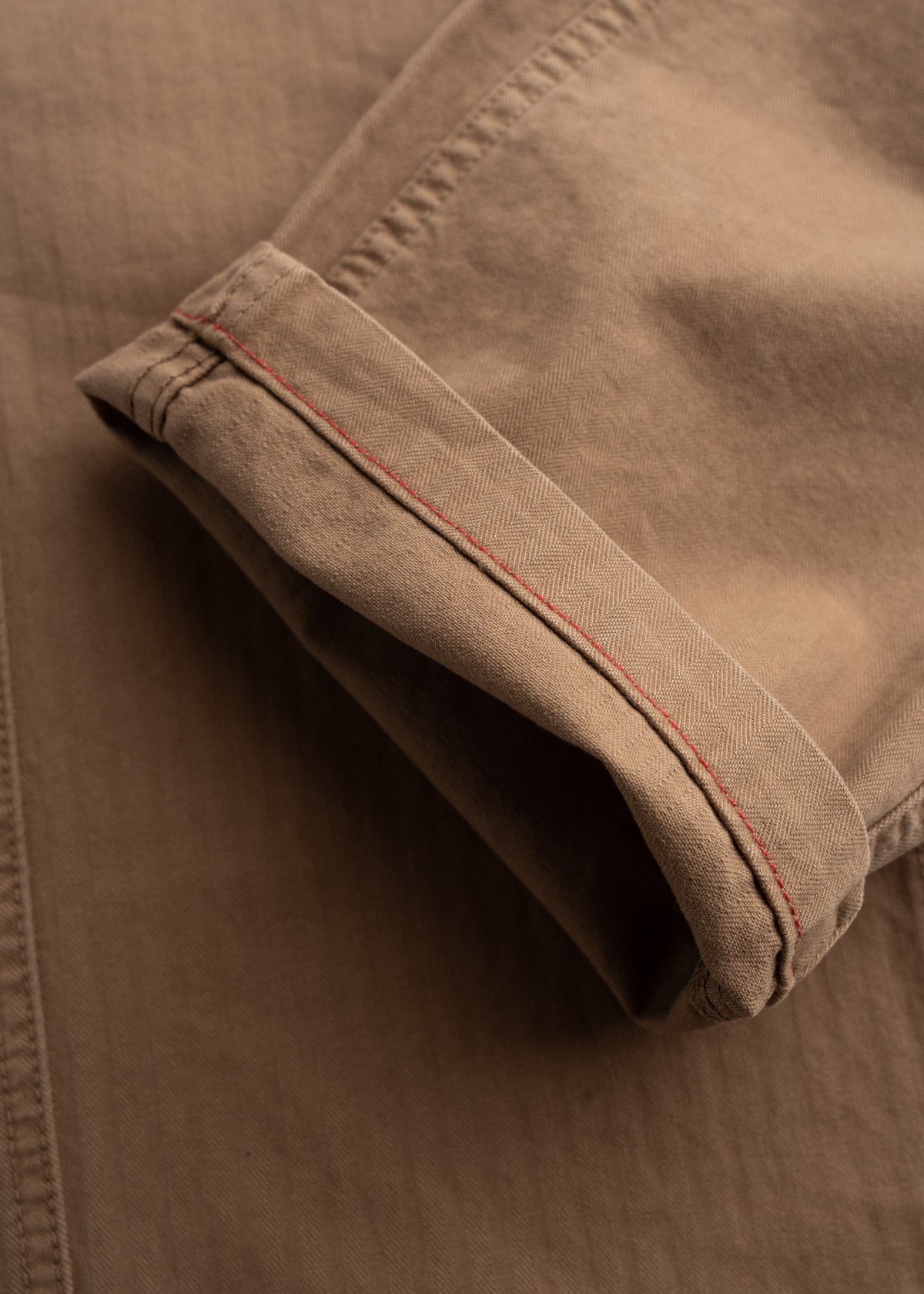 Close-up of a folded khaki fabric with red stitching detail, showcasing texture and craftsmanship in natural light.