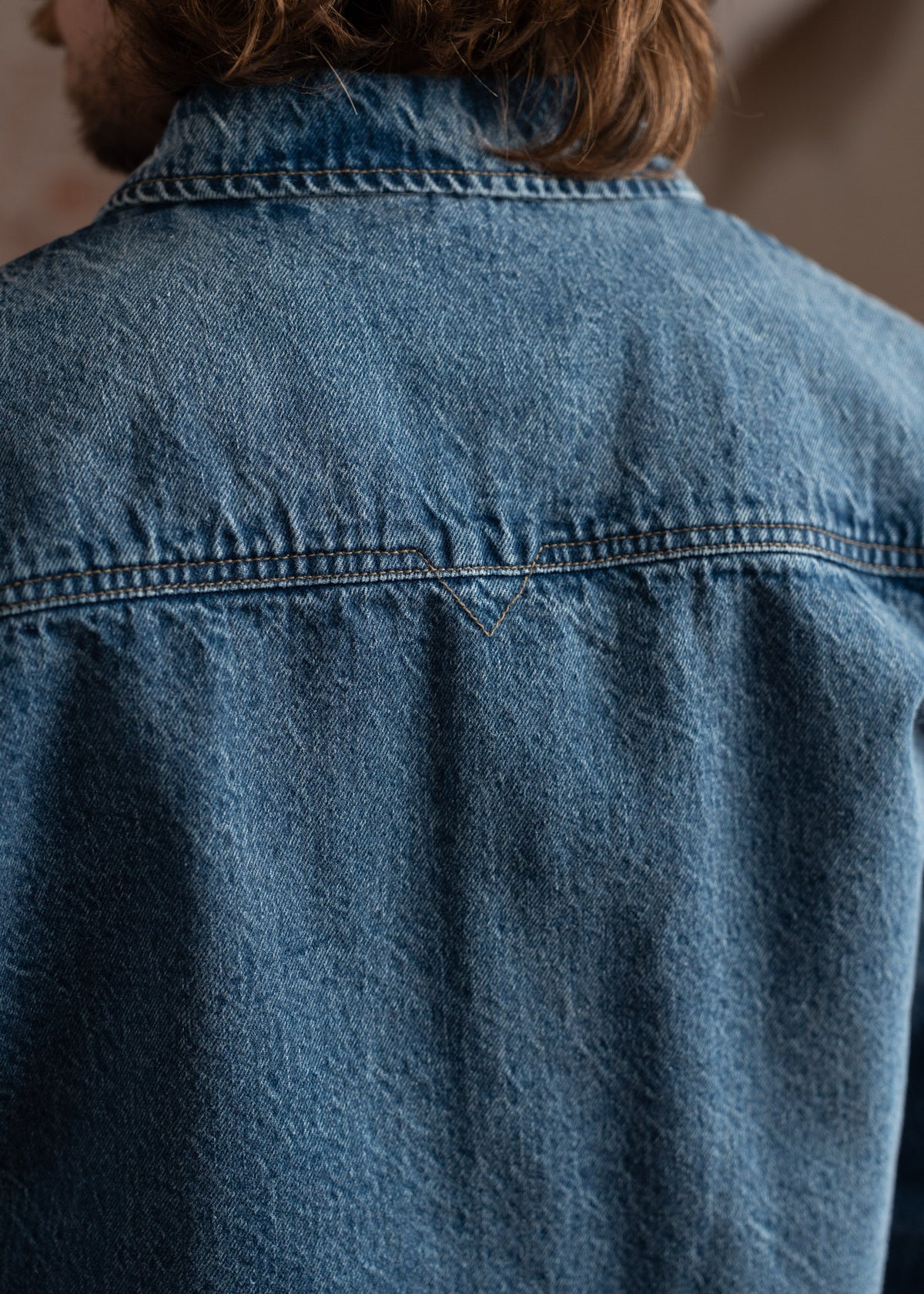 Back view of a person wearing a blue denim jacket with visible stitching, highlighting the texture and casual style.