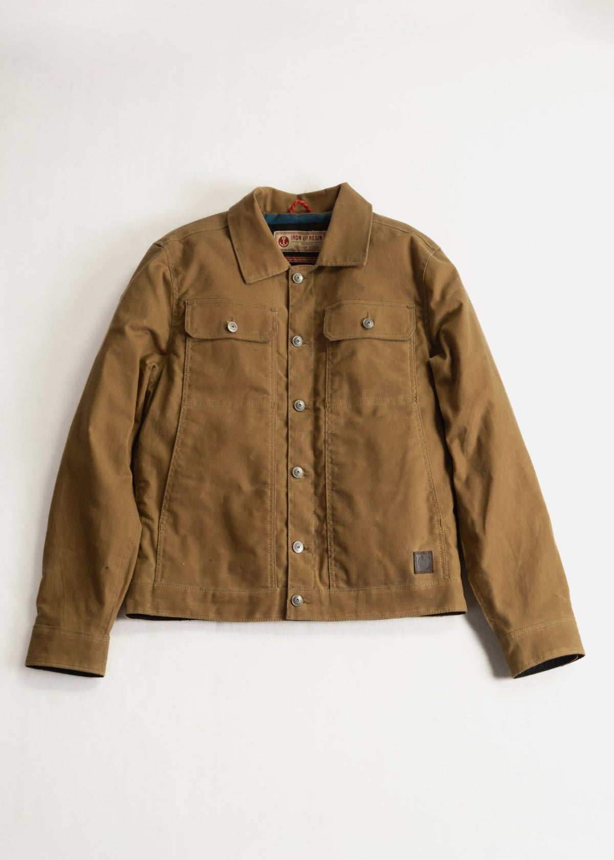 Brown canvas jacket with button closure and two chest pockets, laid flat on a white background. Rugged and stylish design.
