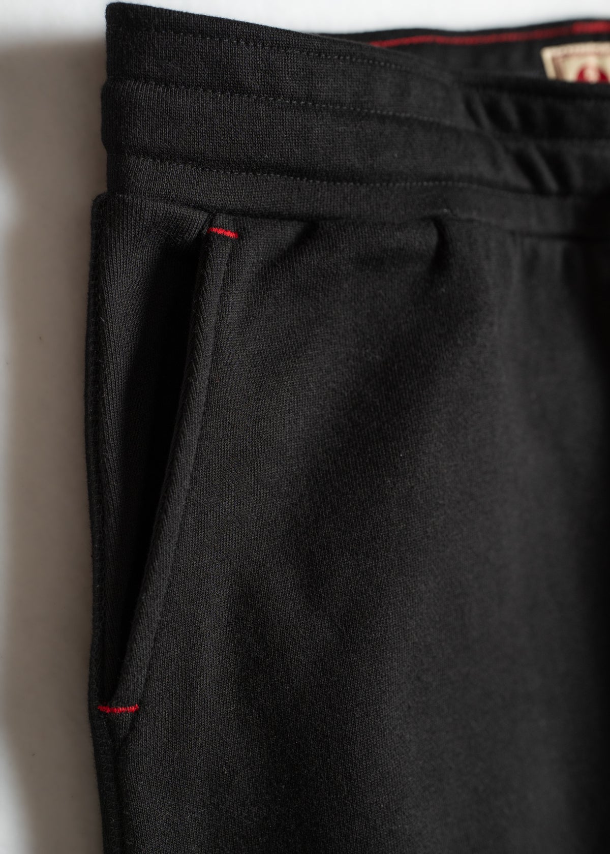 Close-up of black sweatpants with red stitching detail on the pocket, showcasing a simple yet stylish design.