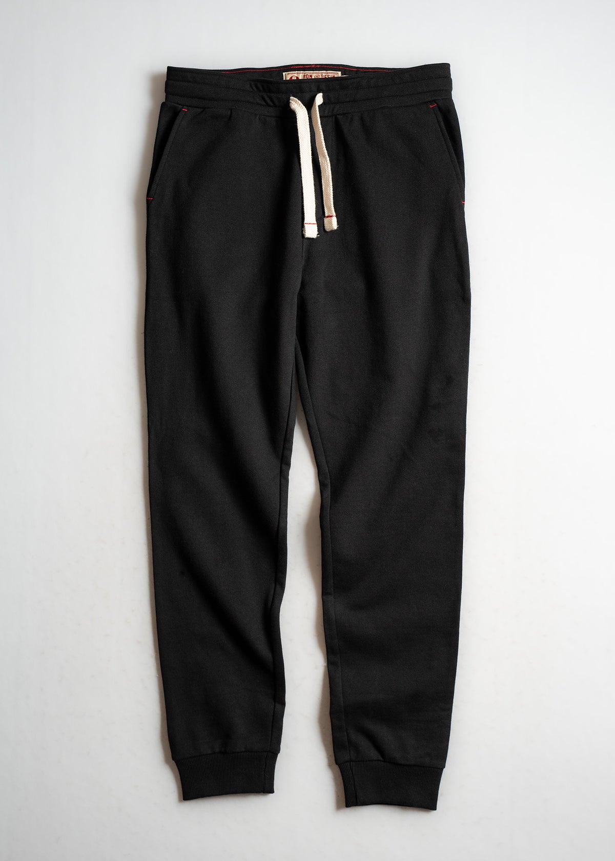 Black jogger pants with white drawstring, elastic cuffs, and side pockets, laid flat on a light background for display.