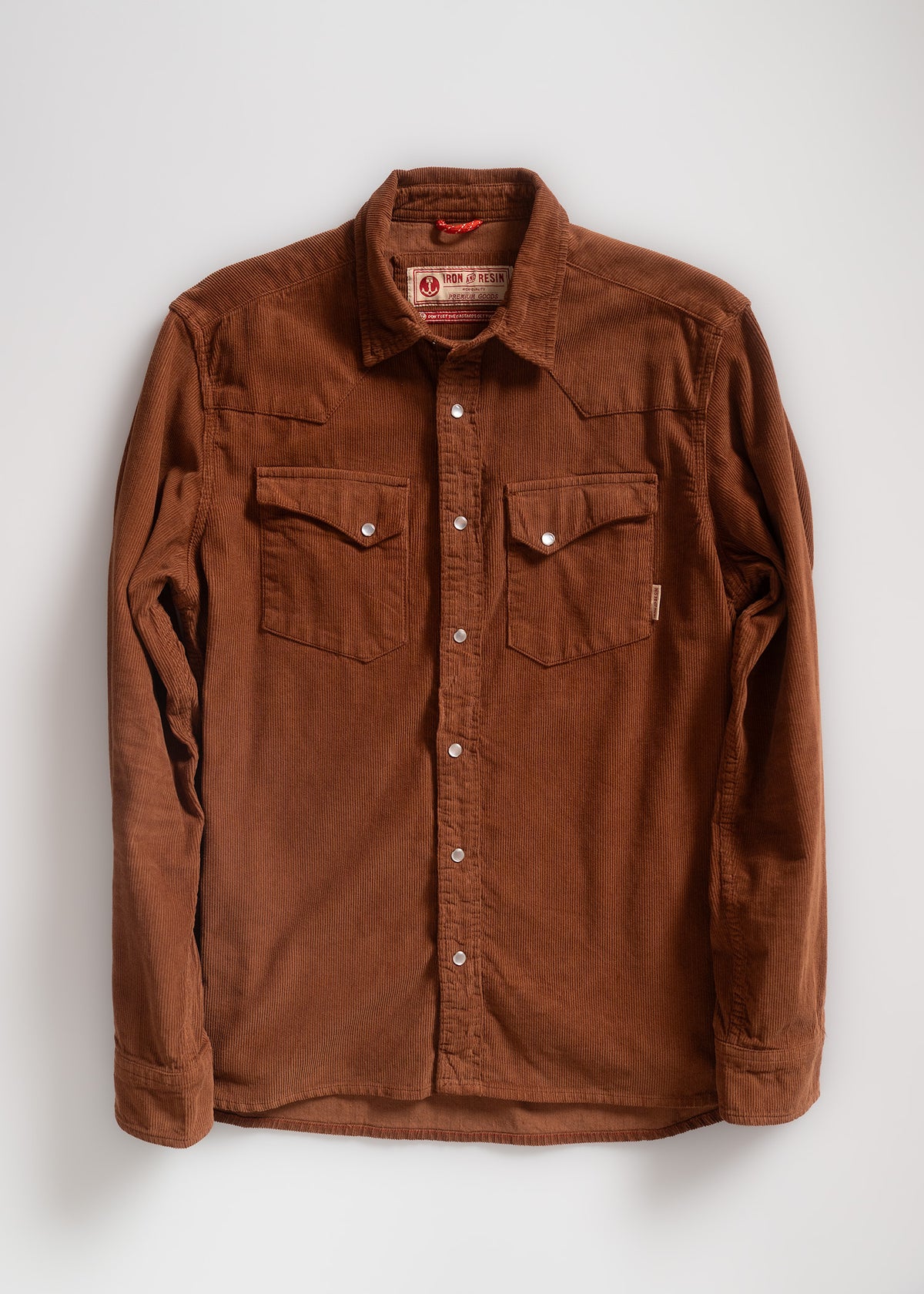 Brown corduroy shirt with buttoned front and two chest pockets, displayed against a plain background, showcasing its texture.