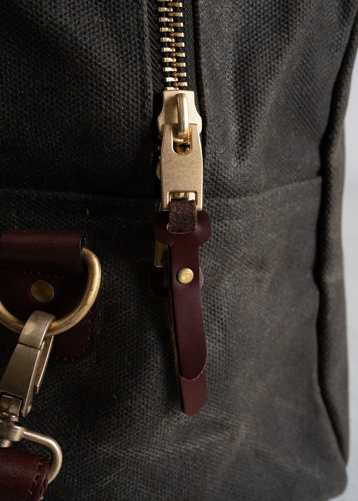 Close-up of a canvas bag showing a brass zipper and leather strap detail, highlighting craftsmanship and material quality.