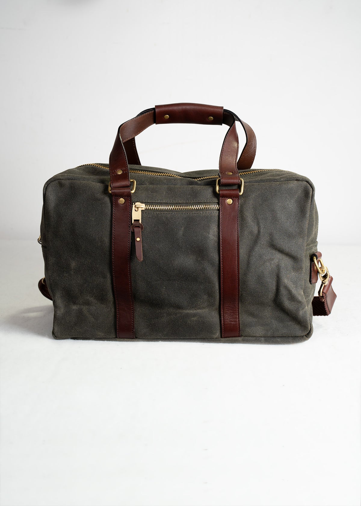 A stylish gray canvas duffel bag with brown leather straps and gold zippers, set against a plain white background.