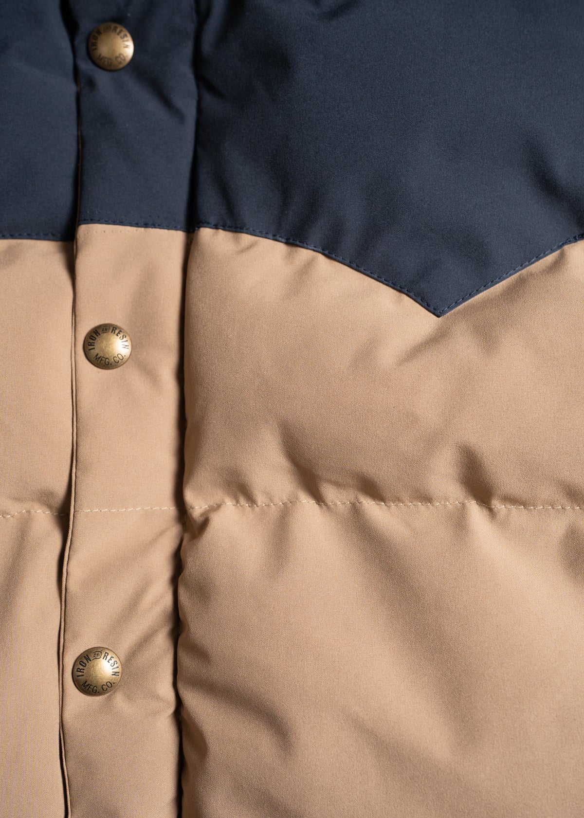 Close-up of a beige and navy puffer jacket with brass buttons, highlighting the texture and color contrast of the fabric.