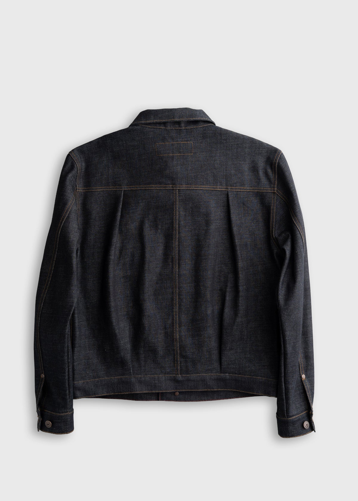Dark denim jacket back view, featuring brown stitching and buttoned cuffs, against a plain light gray background.