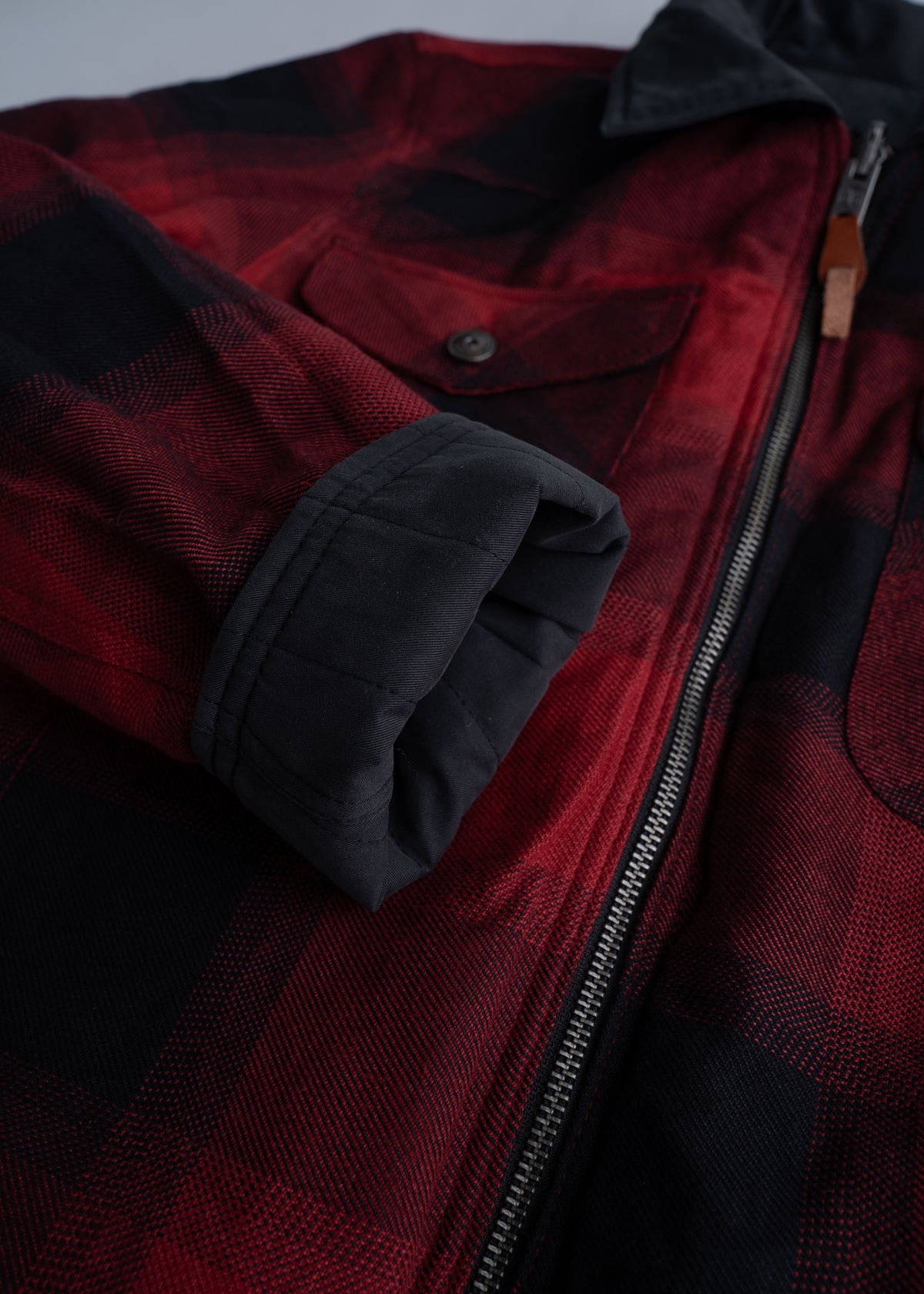 Close-up of a red and black plaid jacket with a zipper and buttoned pocket, showcasing its folded sleeve and fabric texture.