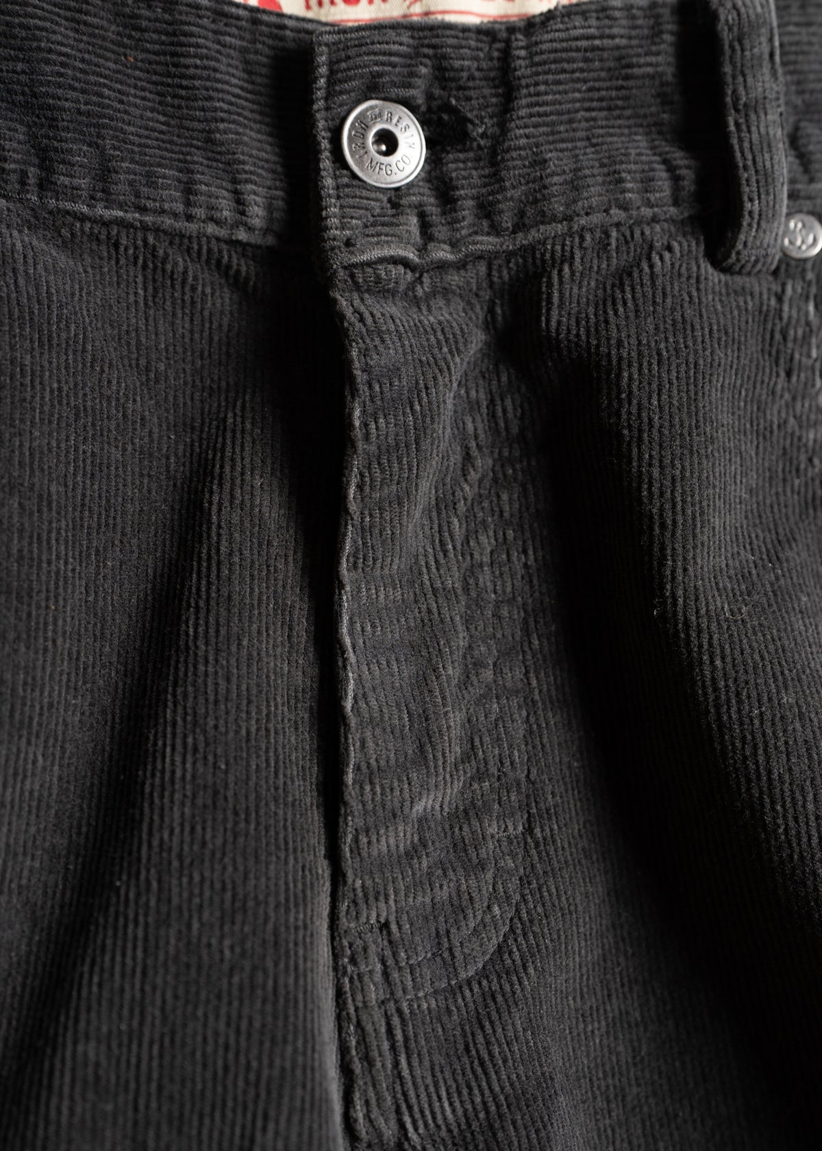 Close-up of black corduroy pants with a visible button and textured fabric, highlighting the detailed stitching and material.