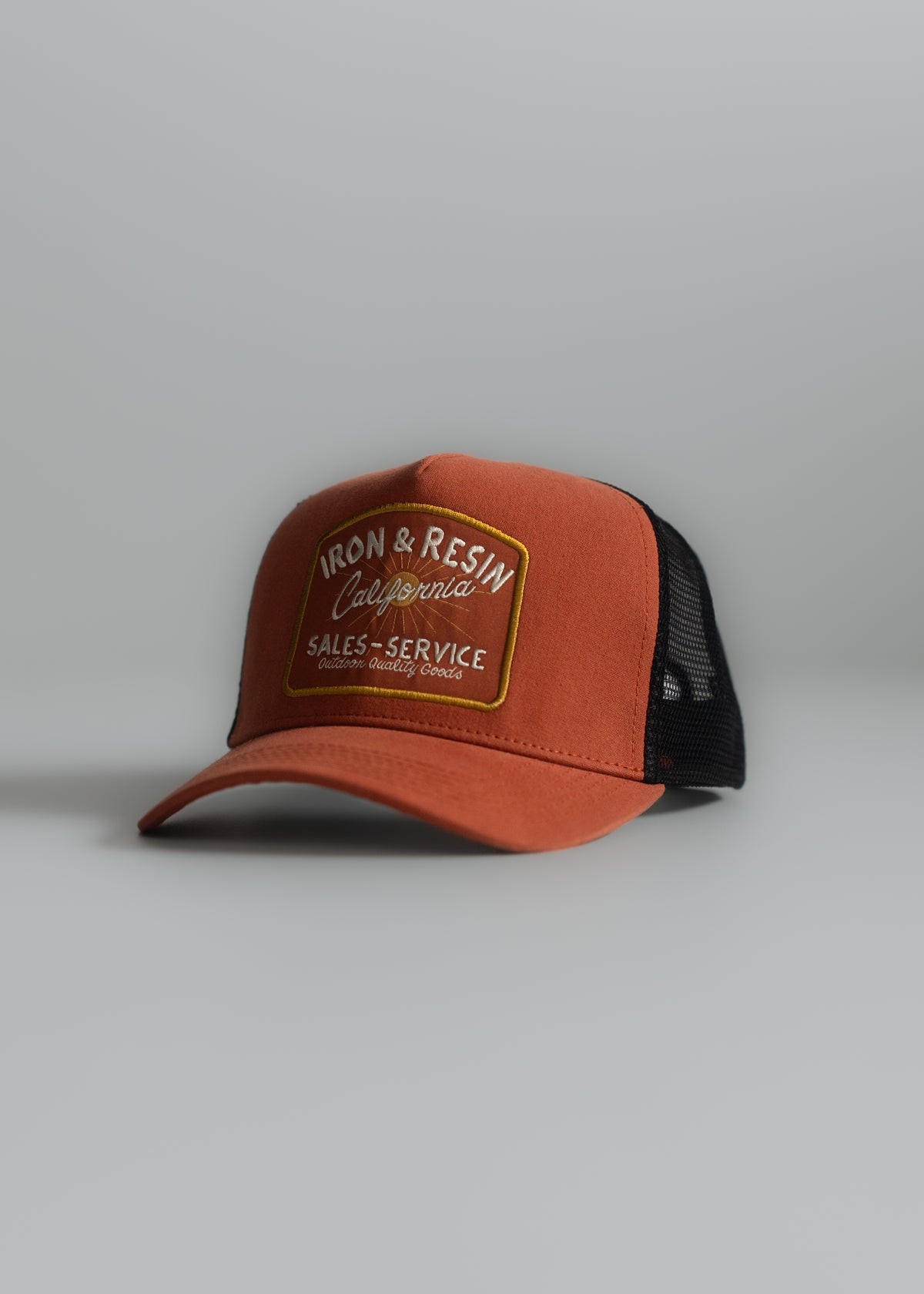 Orange cap with "Iron & Resin California Sales Service" patch, black mesh back, on a gray surface. Casual and stylish design.