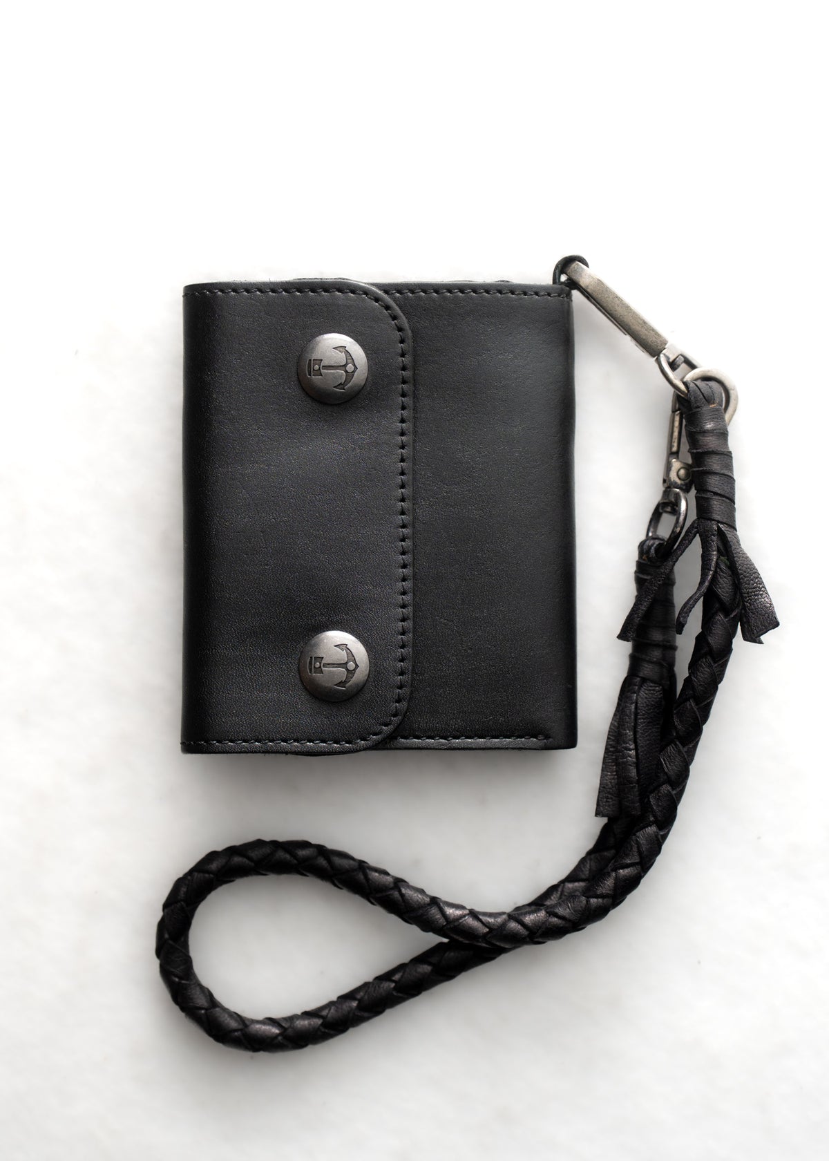 Black leather wallet with metal buttons and braided strap on white background, showcasing sleek design and functionality.