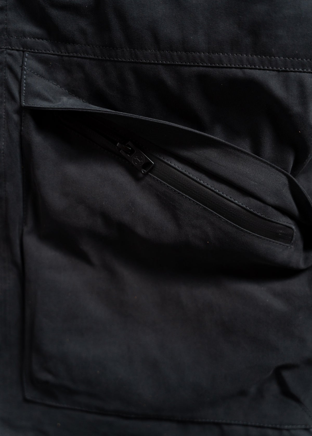 Close-up of a black jacket pocket with a visible zipper, showcasing the texture and stitching details of the fabric.