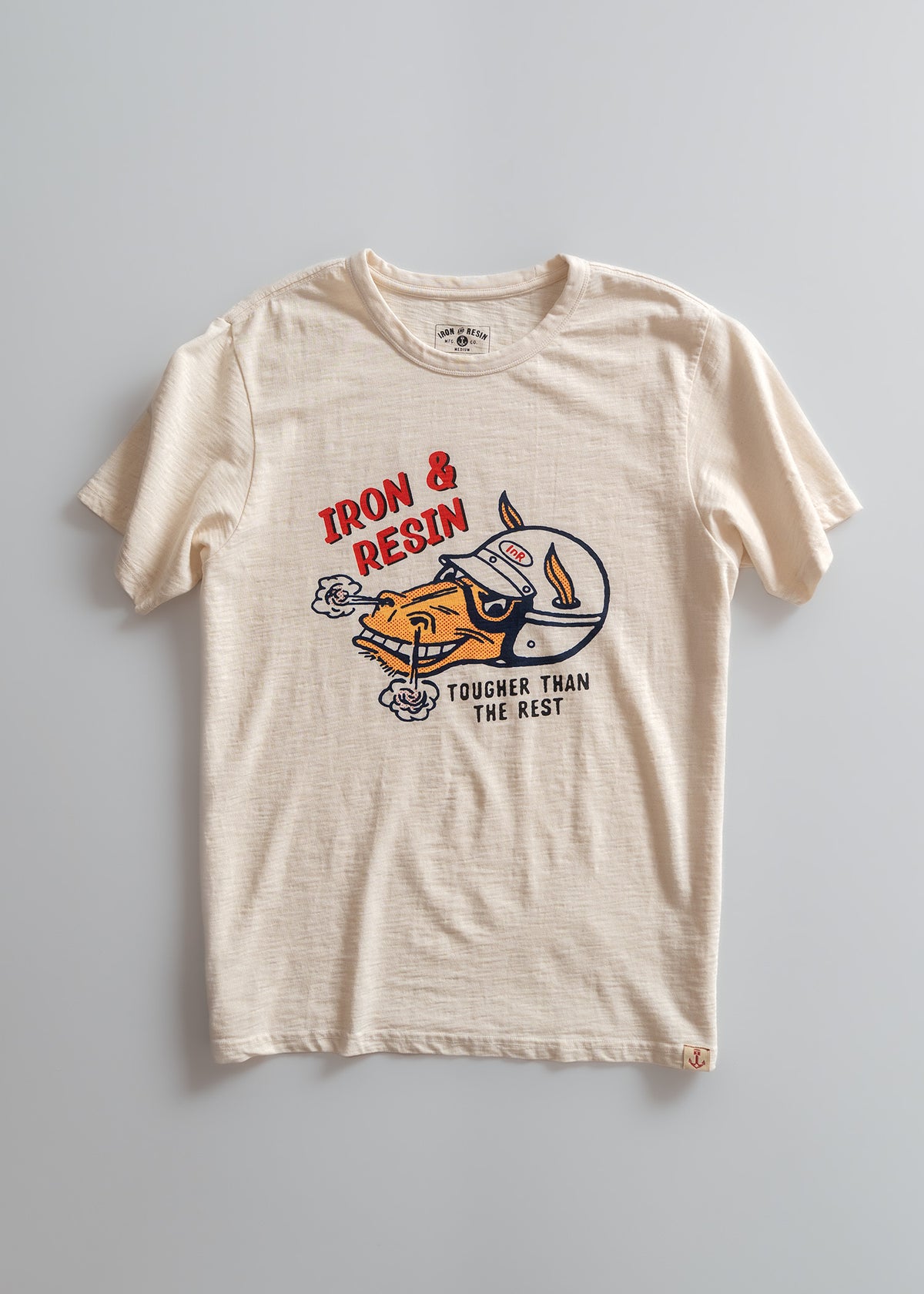 Beige t-shirt with "Iron & Resin" text and a graphic of a helmeted figure, captioned "Tougher Than The Rest" on the front.