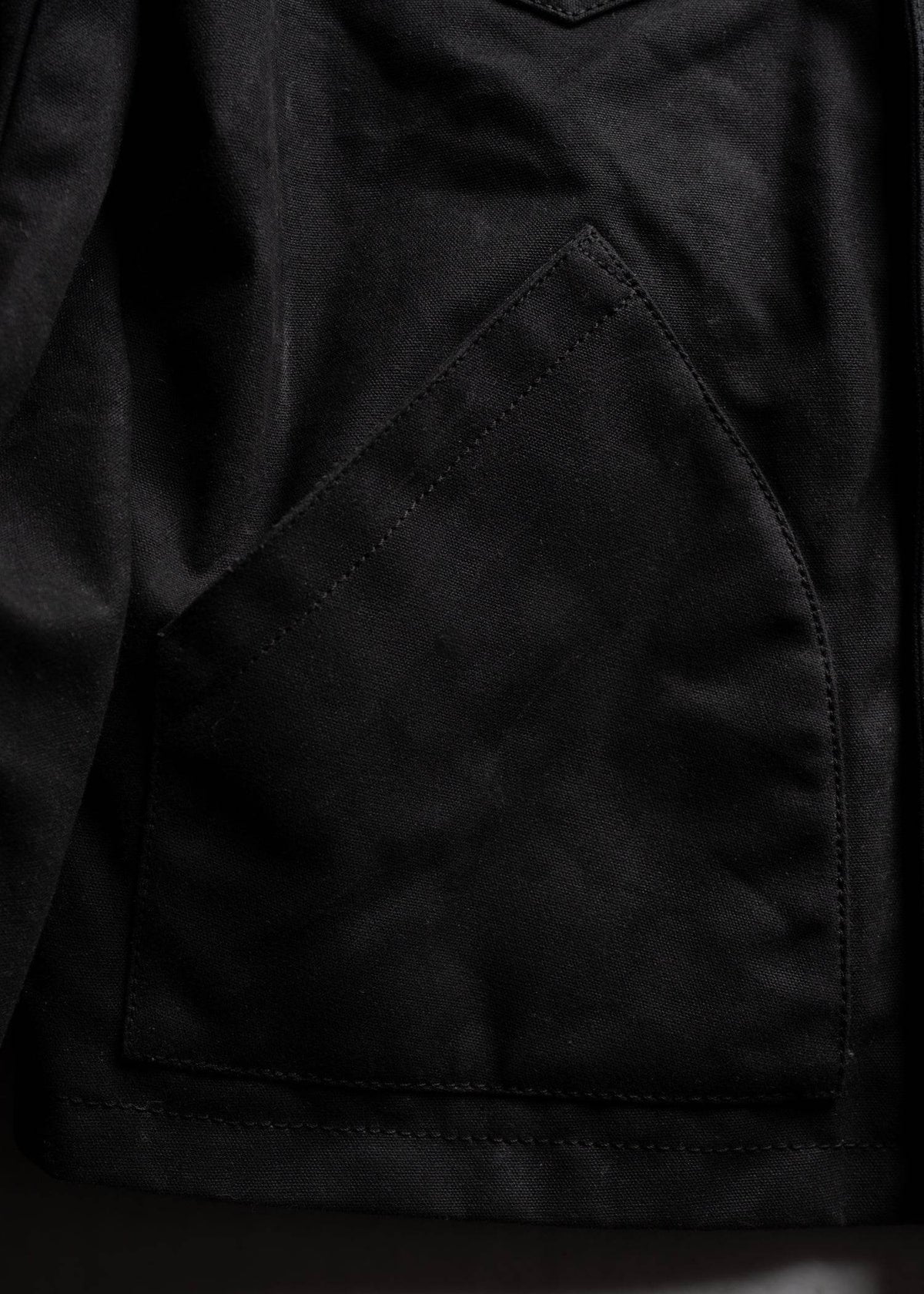 Close-up of a black jacket pocket with visible stitching, highlighting the texture and craftsmanship of the fabric.