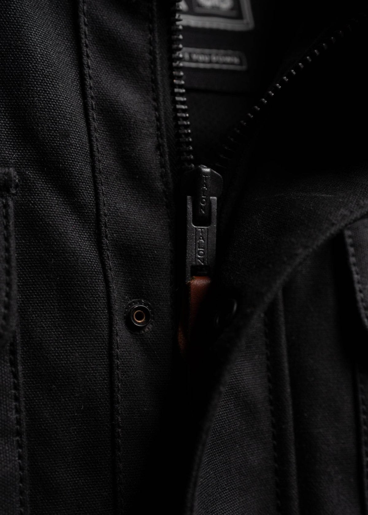 Close-up of a black jacket zipper, partially open, revealing a hint of brown fabric beneath, highlighting texture and detail.