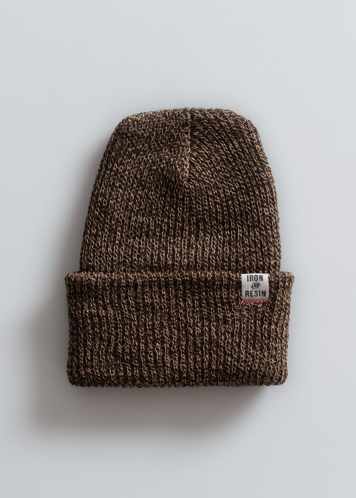 Brown knit beanie with a folded brim and "Iron and Resin" label on a light gray background, showcasing texture and style.