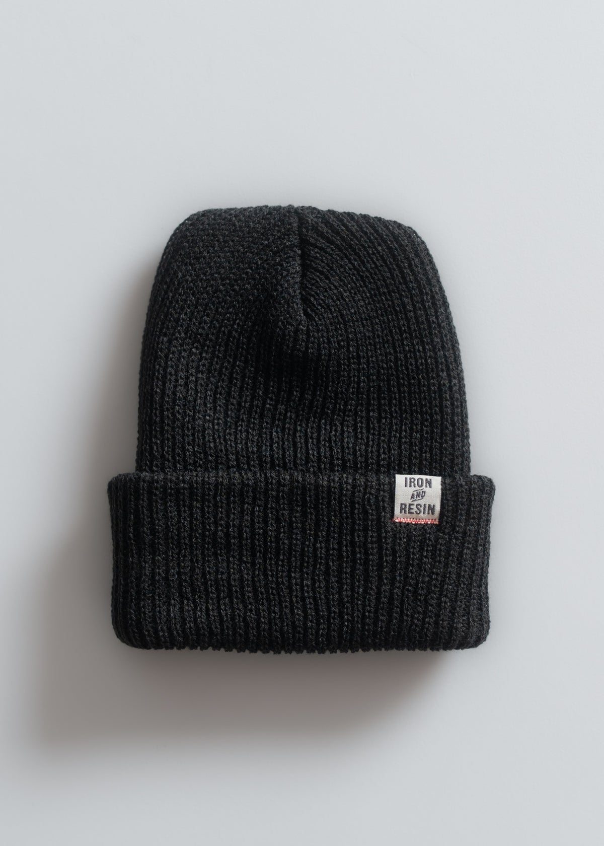 A black knit beanie with a folded brim, featuring an "Iron and Resin" label on a plain white background.