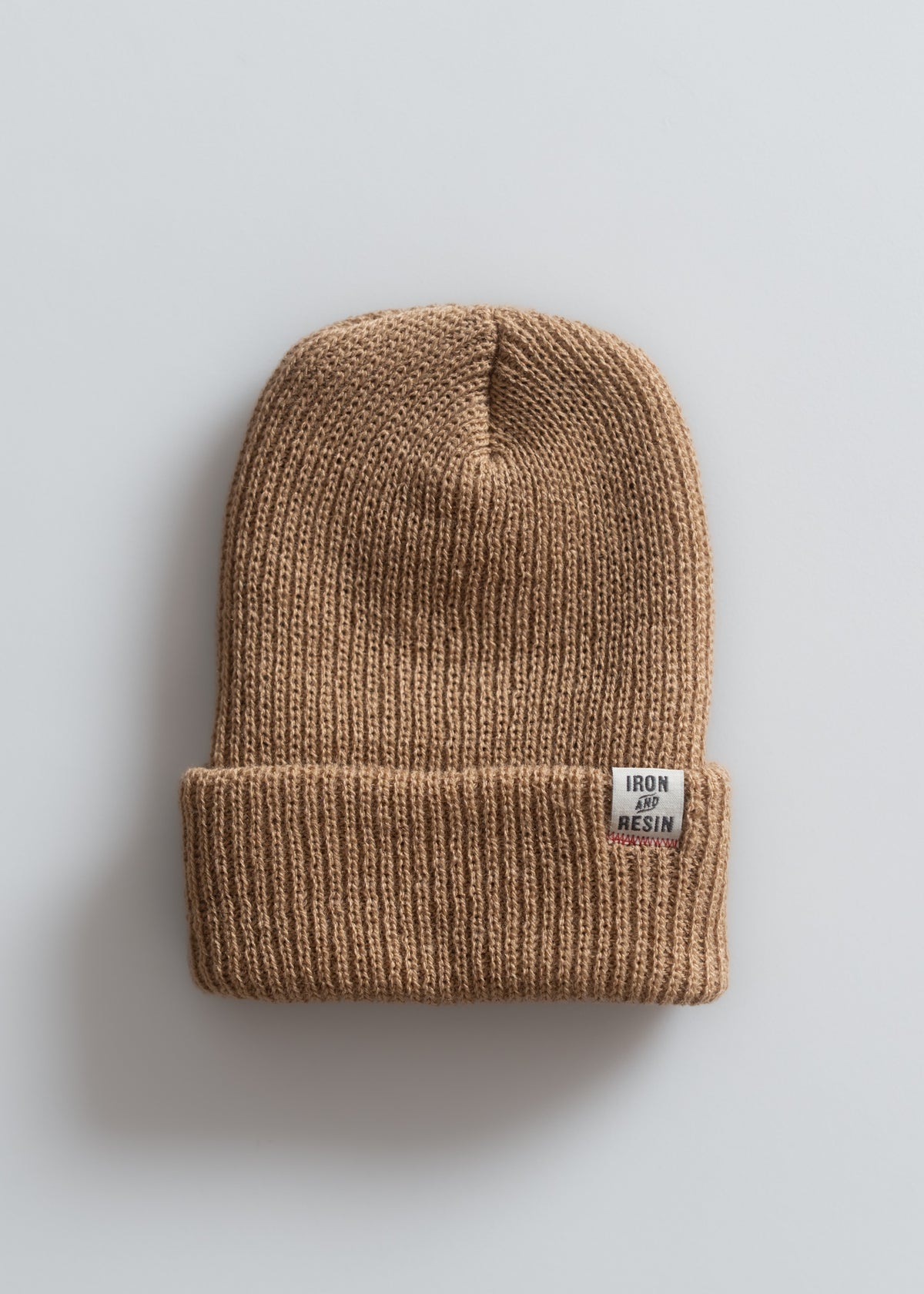 A brown knit beanie with a folded brim and "Iron and Resin" label, displayed on a light gray background.