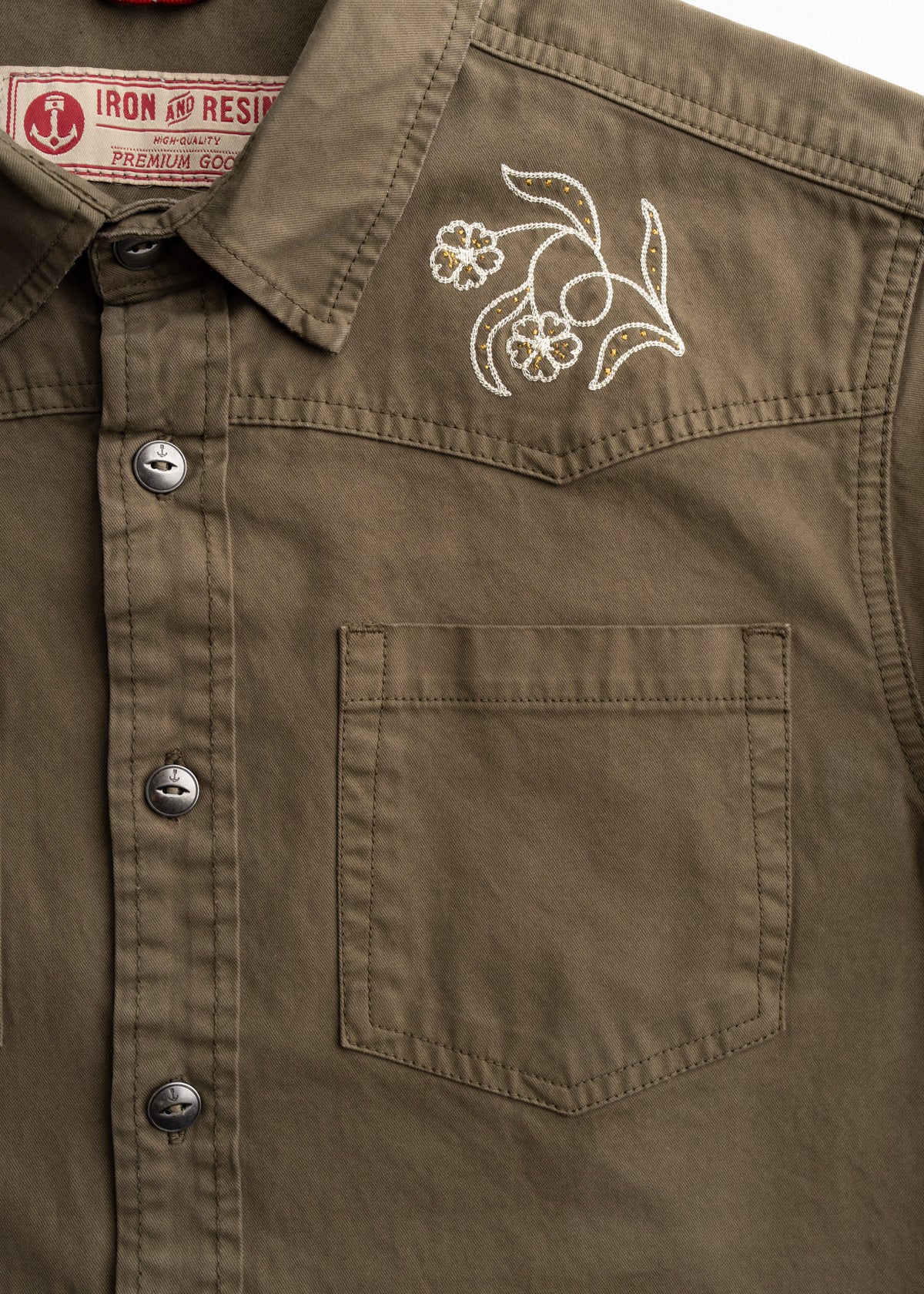 Khaki shirt with floral embroidery on the shoulder, featuring a front pocket and metal buttons. Iron and Resin label visible.