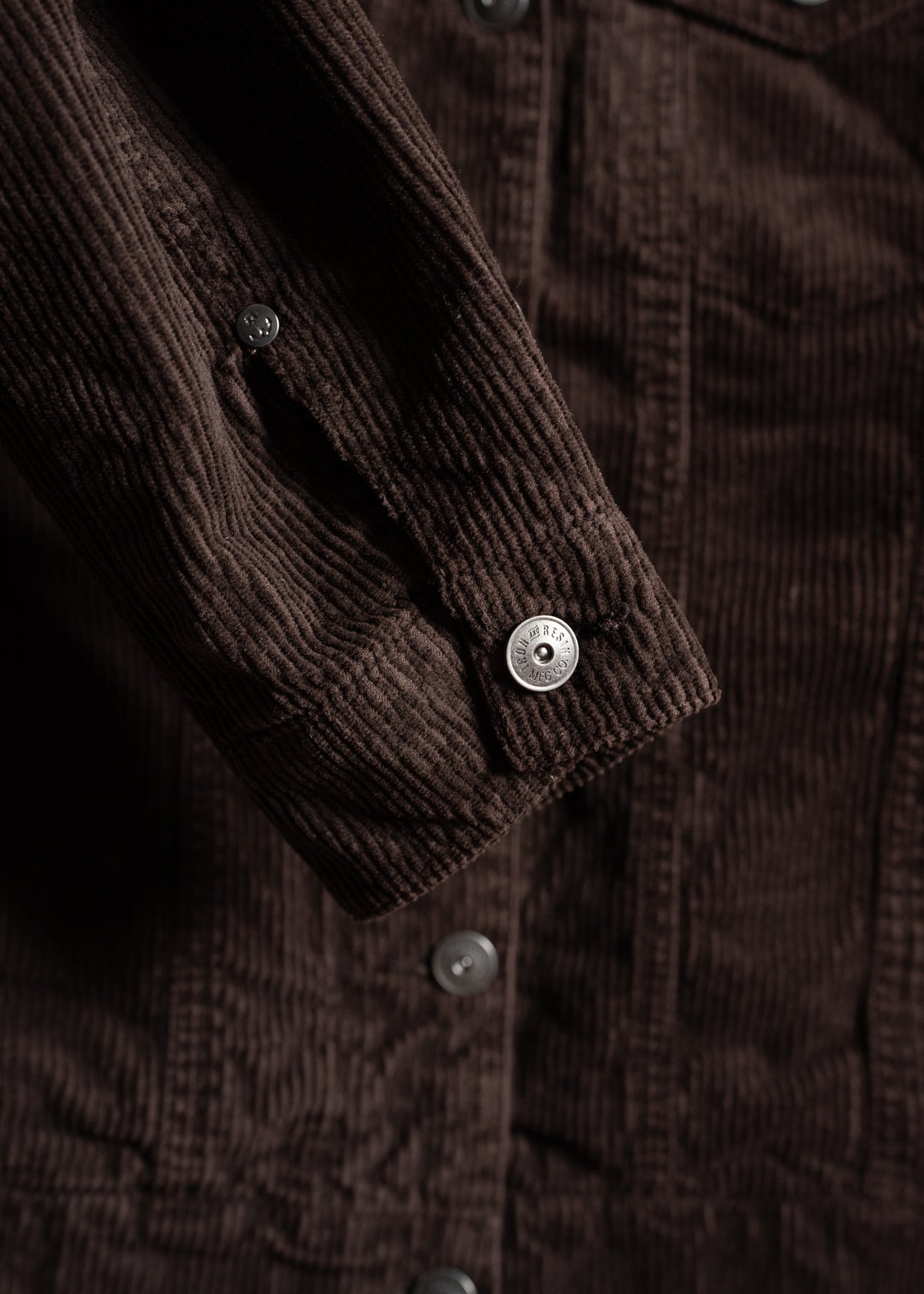 Close-up of a brown corduroy jacket sleeve with a silver button, highlighting the texture and button details.