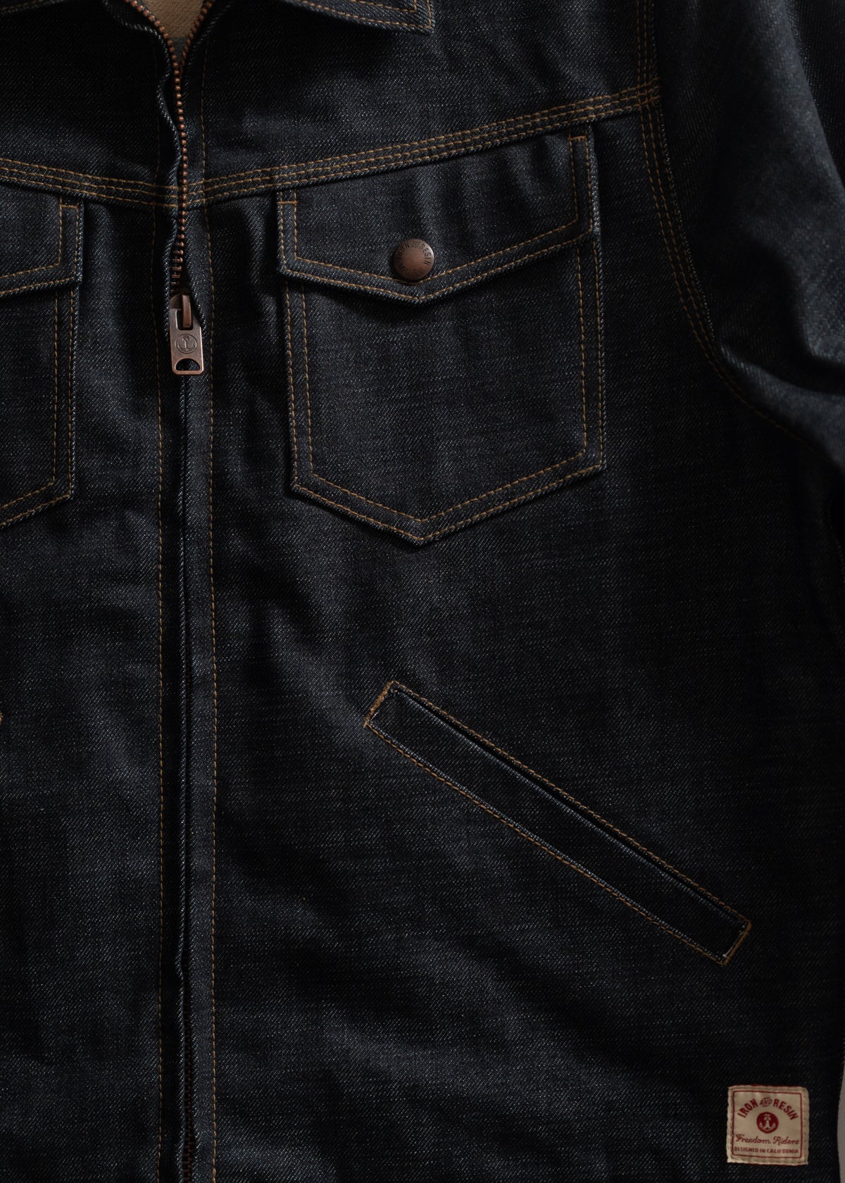 Dark denim jacket with front zipper, two chest pockets with buttons, and a small label at the bottom right corner.