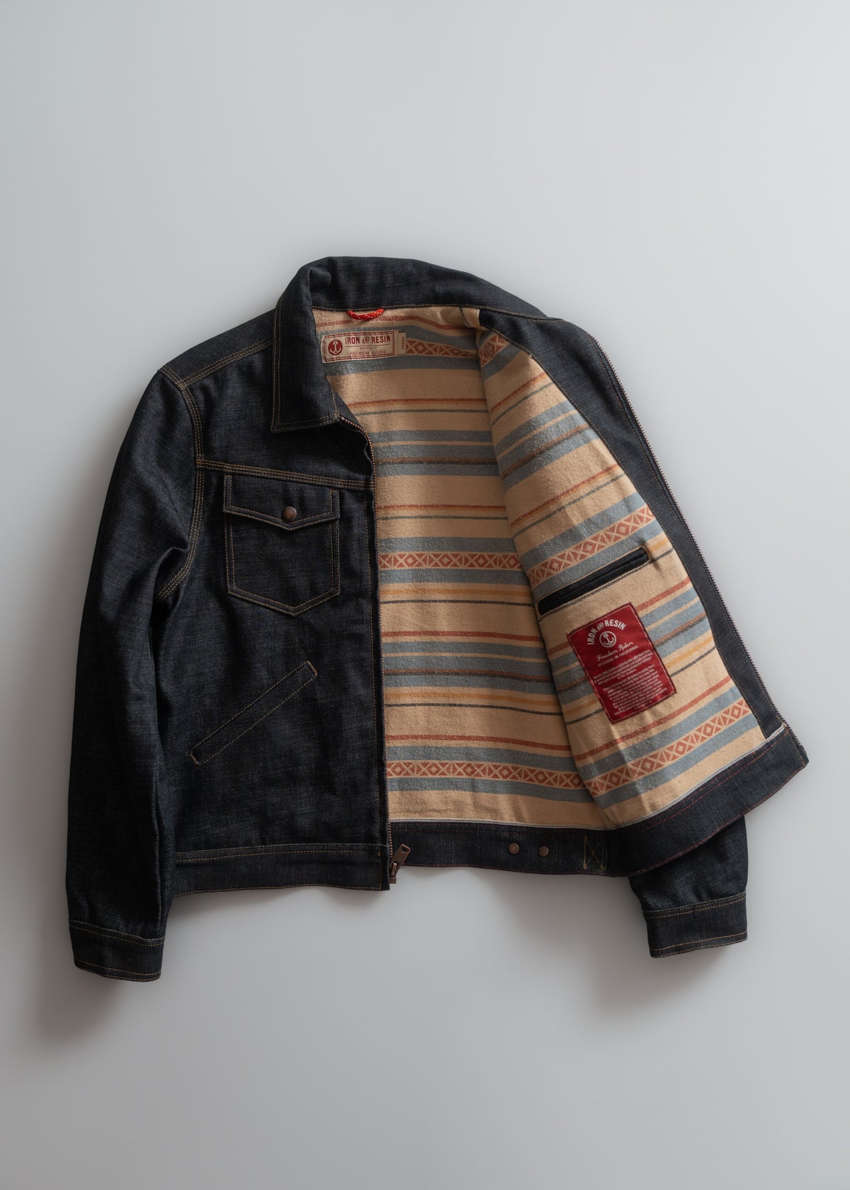 Denim jacket with open front reveals striped, patterned lining in beige, blue, and red. A red label is visible inside.