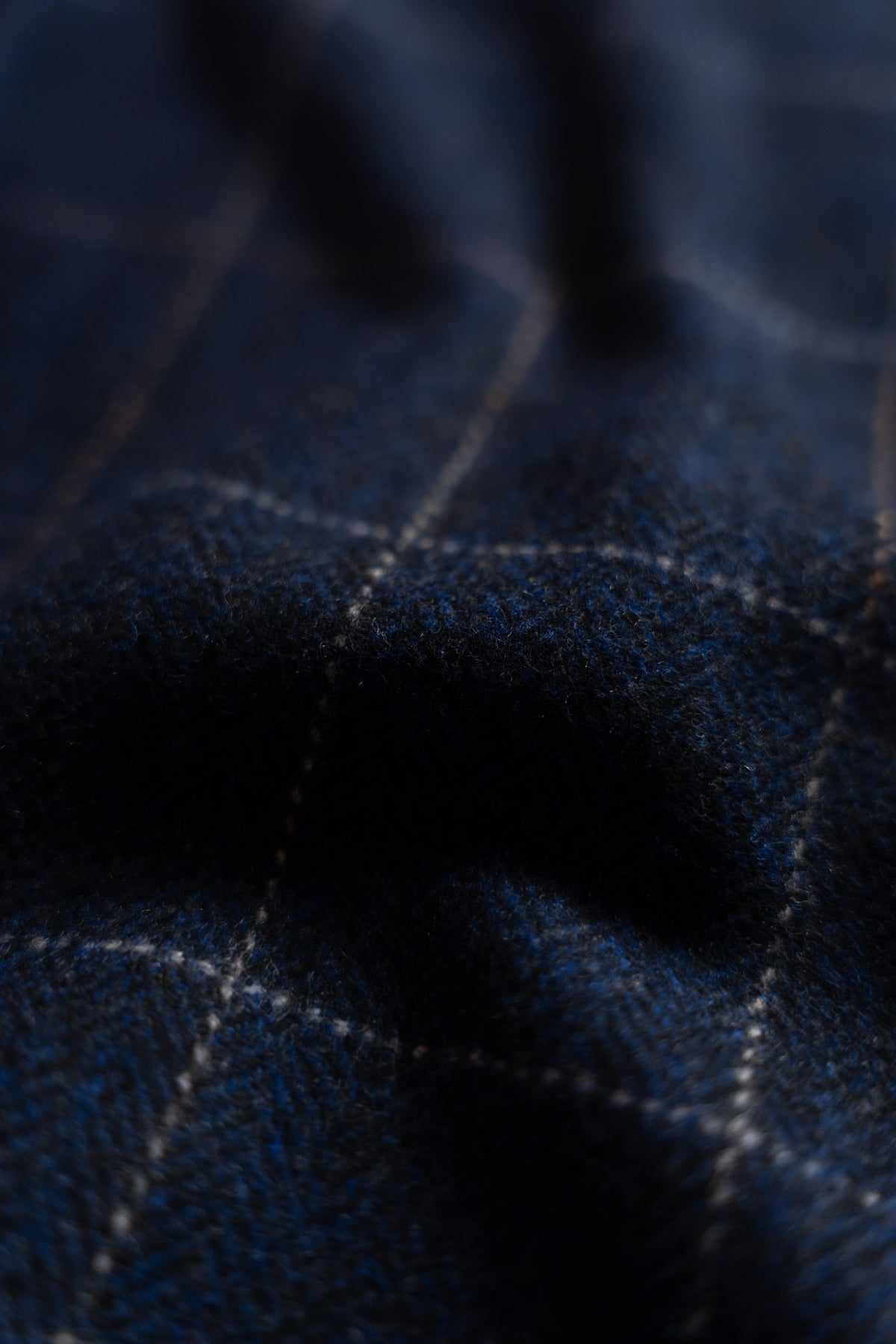 Close-up of dark blue plaid fabric with soft texture and subtle white lines, creating a cozy and elegant pattern.