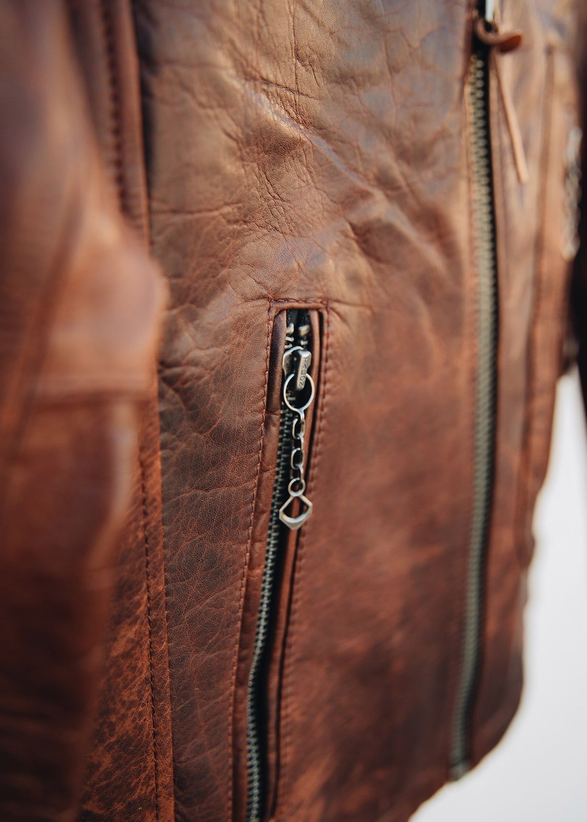 Close-up of a brown leather jacket with a detailed zipper and textured surface, highlighting its rugged and stylish design.