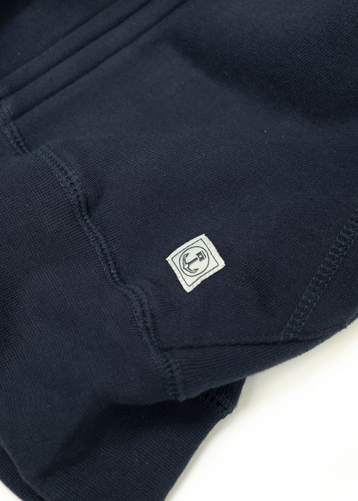 Close-up of a navy blue sweatshirt sleeve featuring a small white anchor logo patch near the cuff, highlighting its detail.