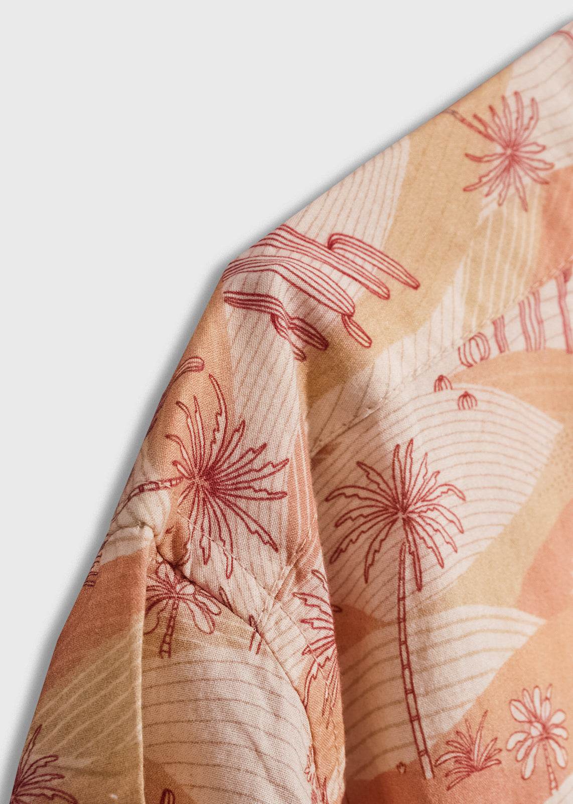 Close-up of a shirt with a tropical palm tree pattern in red and beige tones, showcasing intricate fabric design details.