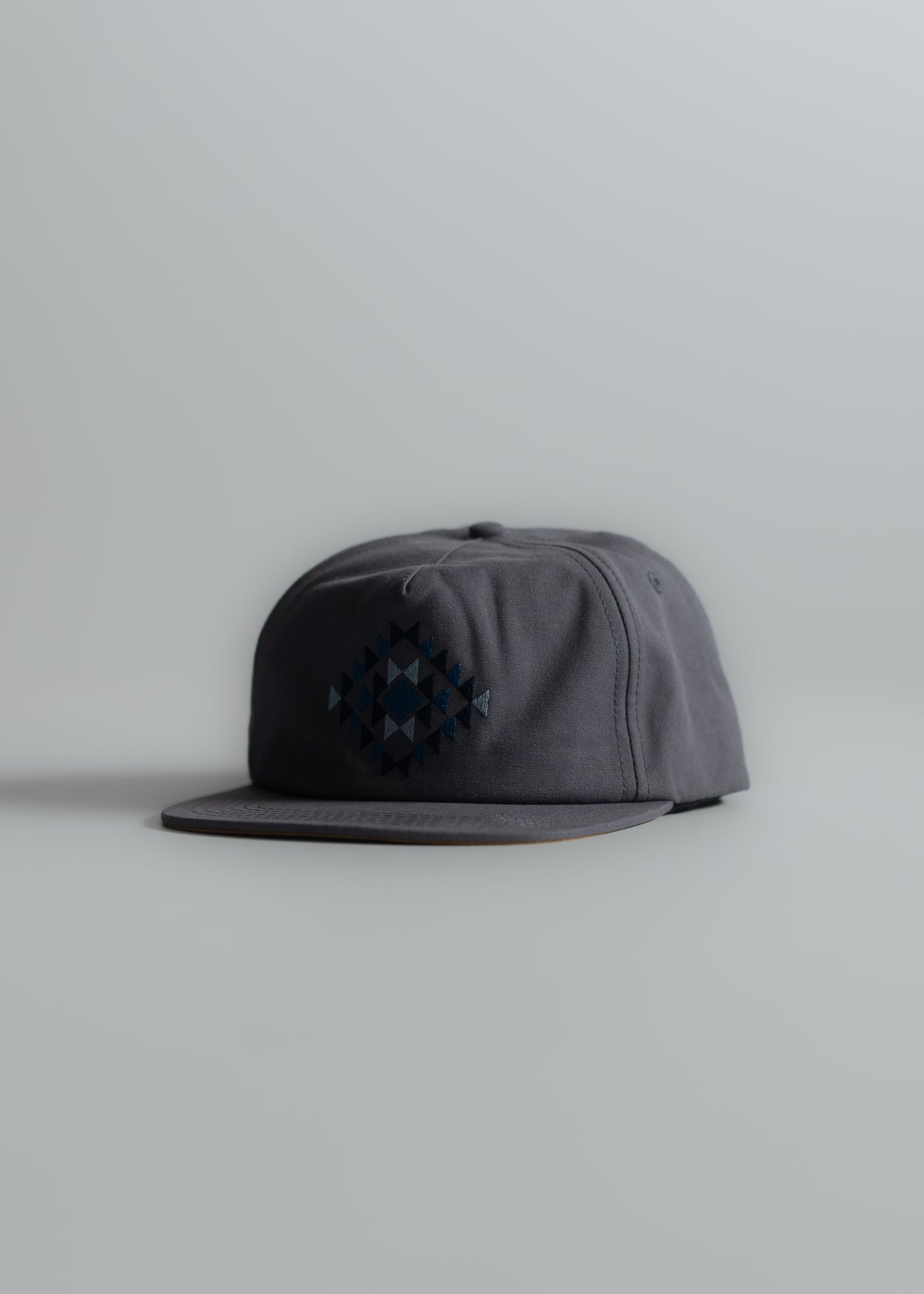 Gray baseball cap with geometric pattern on front, placed on a light gray surface, showcasing minimalist design and style.