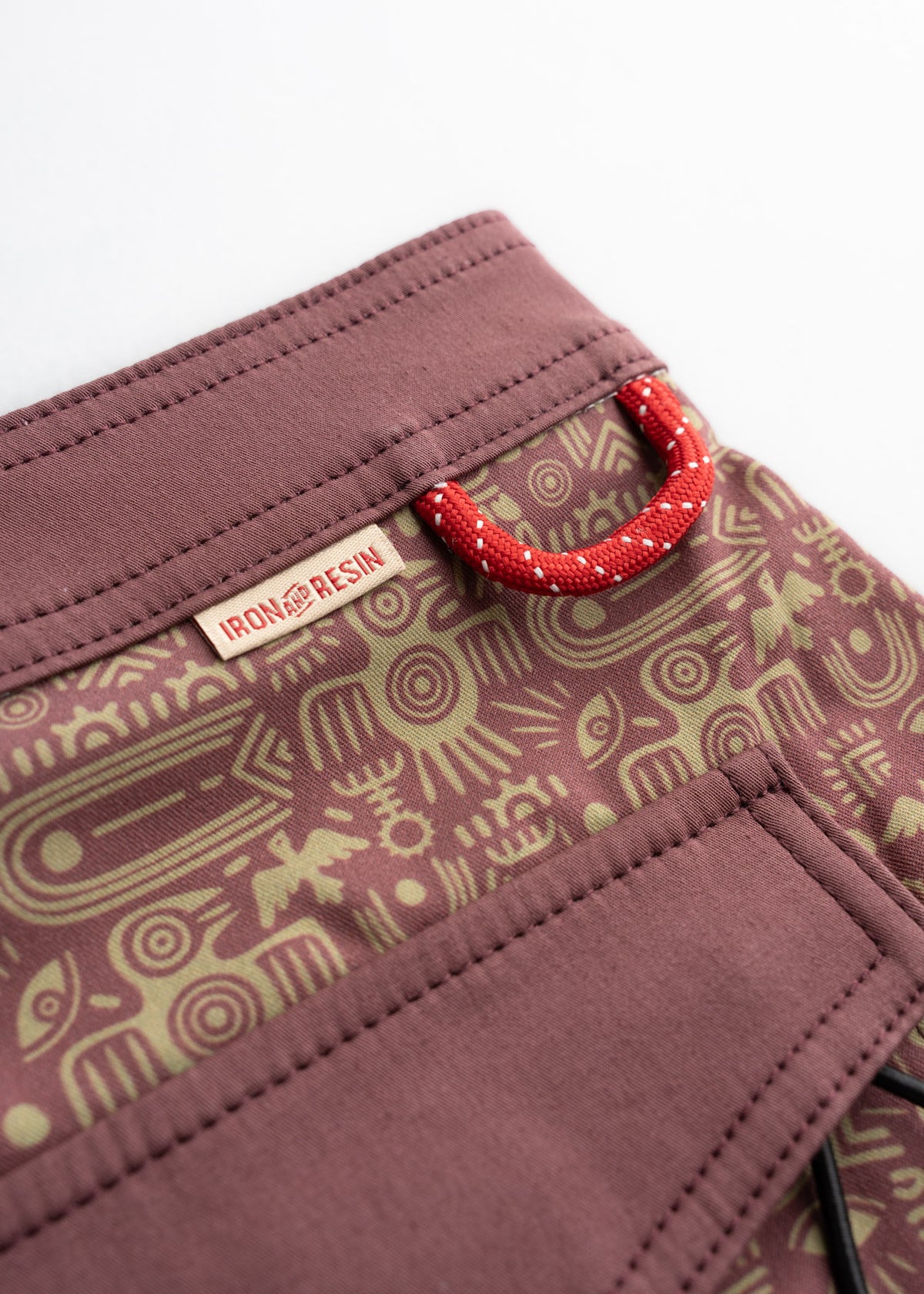 Close-up of Iron & Resin fabric with tribal patterns and a red loop. The design features intricate symbols on a muted background.