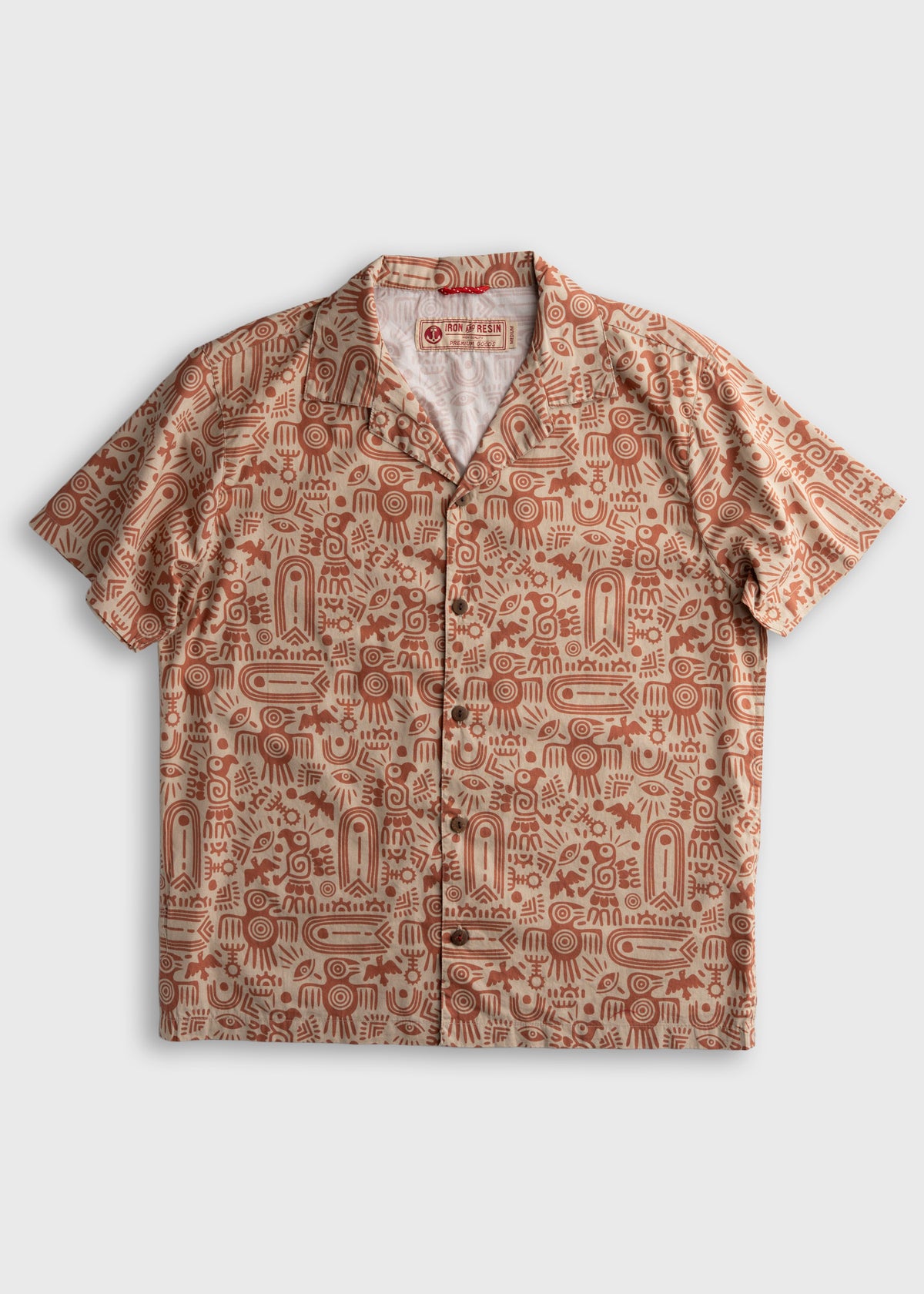 Short-sleeve shirt with red tribal patterns on beige fabric, featuring a button-up front and collar, laid flat on a white background.