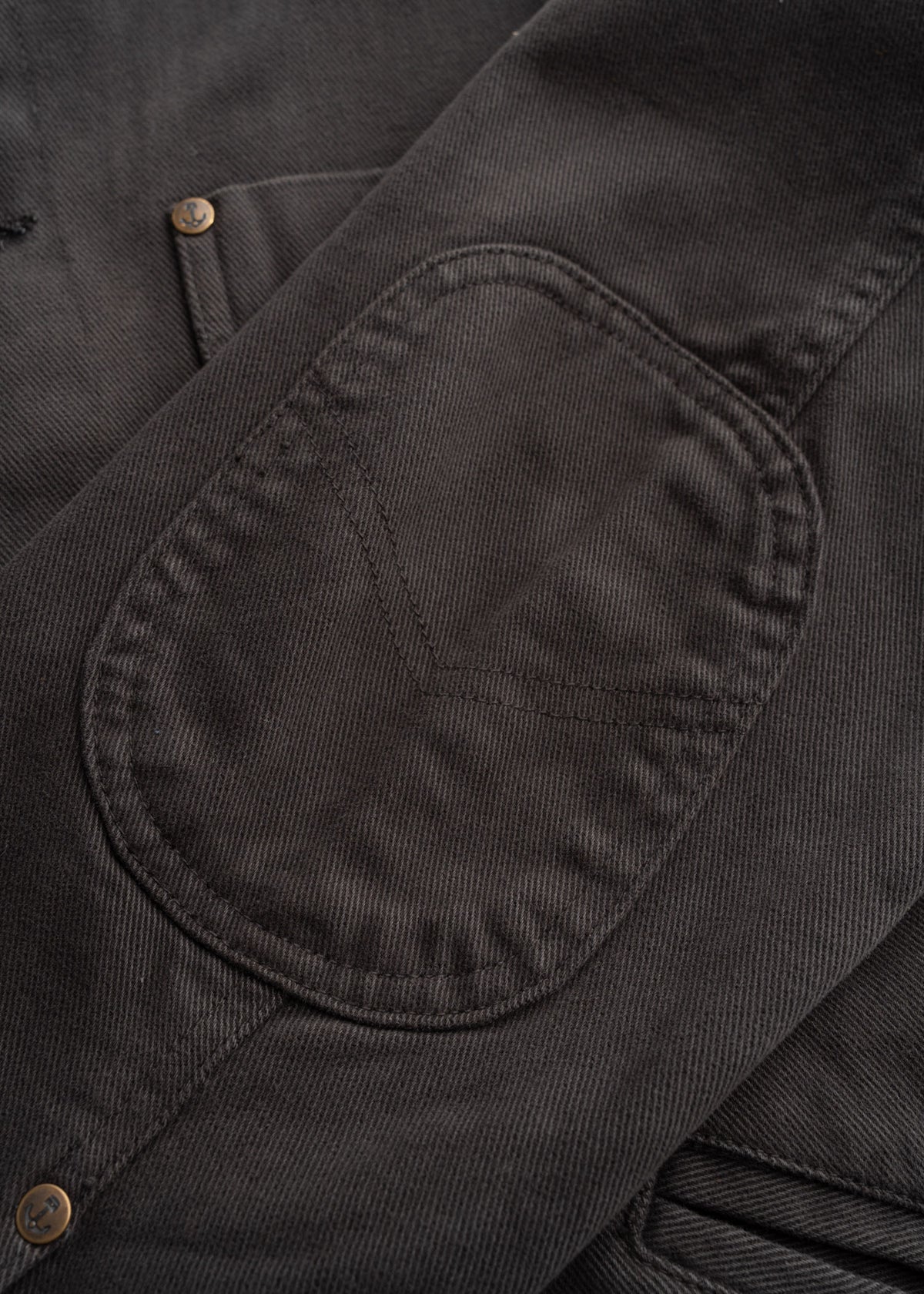 Close up of peach bull denim fabric showing, custom buttons, detailed stitching, custom buttons, textured cotton weave and durable workwear construction
