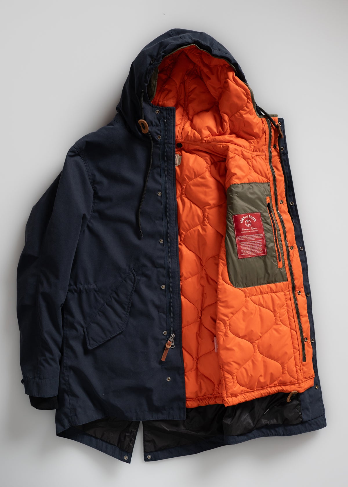 Navy parka with orange quilted lining, hood, and pockets, displayed open to reveal interior details and label on a light background.