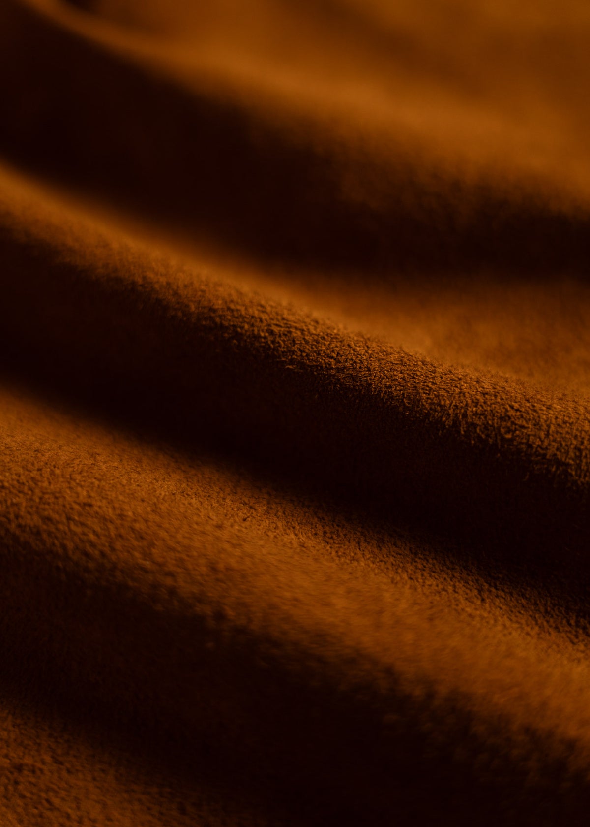 Close-up of soft, textured brown fabric with gentle folds, creating a warm and cozy appearance under soft lighting.
