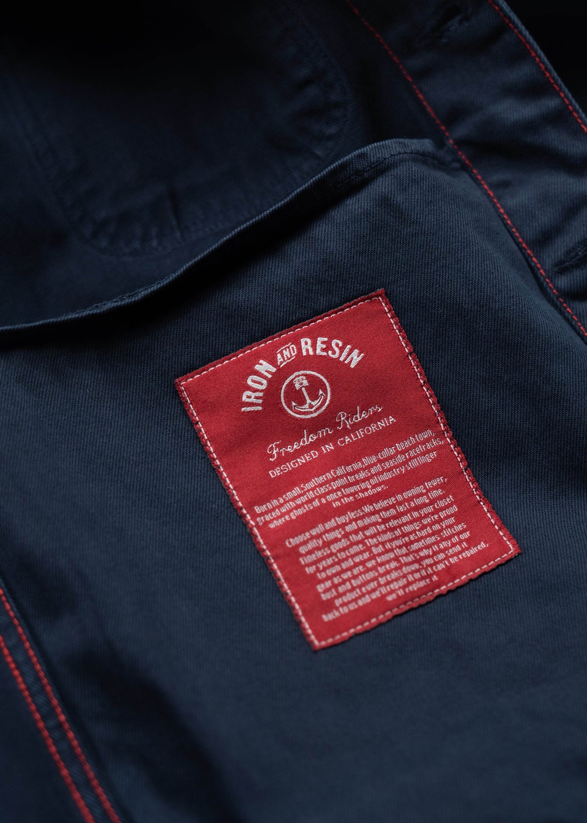 Close-up of a red "Iron and Resin" label on a dark fabric, highlighting "Freedom Riders" and "Designed in California" text.