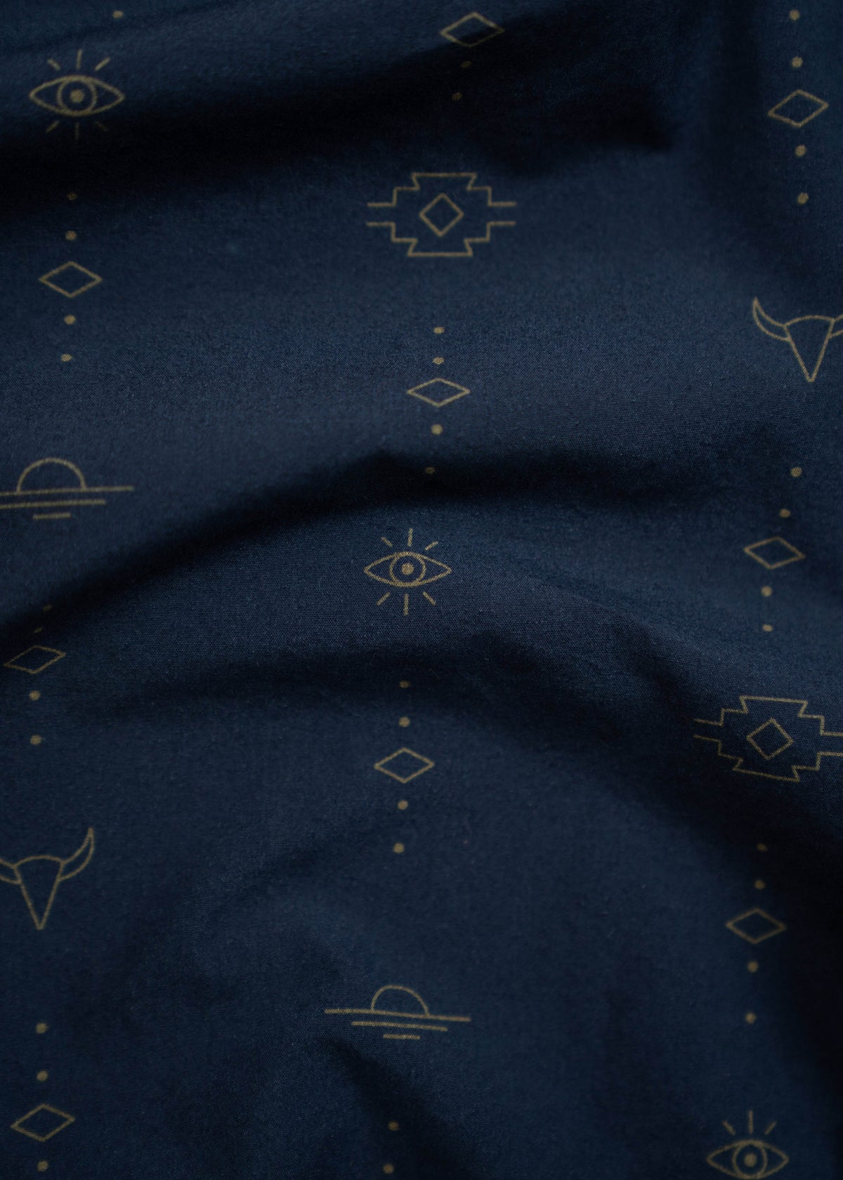 Dark blue fabric with gold geometric patterns, including eyes, diamonds, and lines, creating a mystical, abstract design.