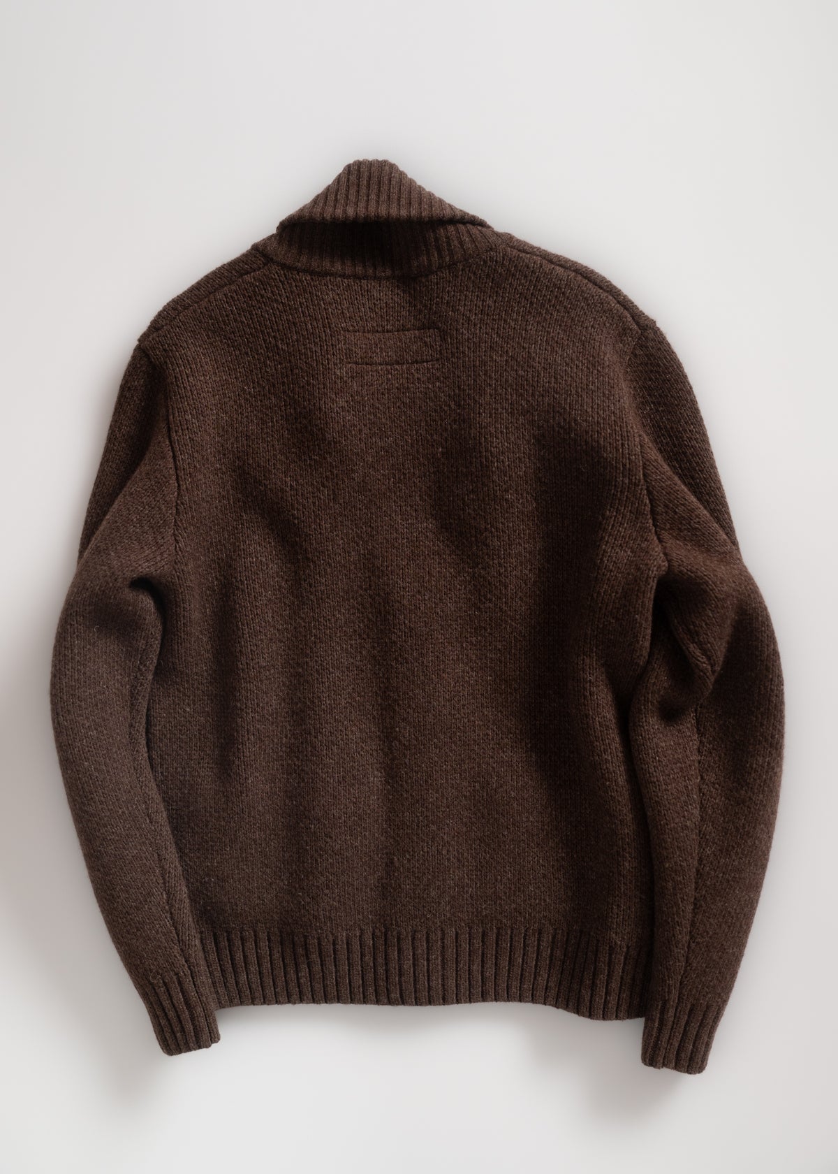 Brown knit sweater with ribbed cuffs and collar, laid flat on a white background, showcasing its texture and design.