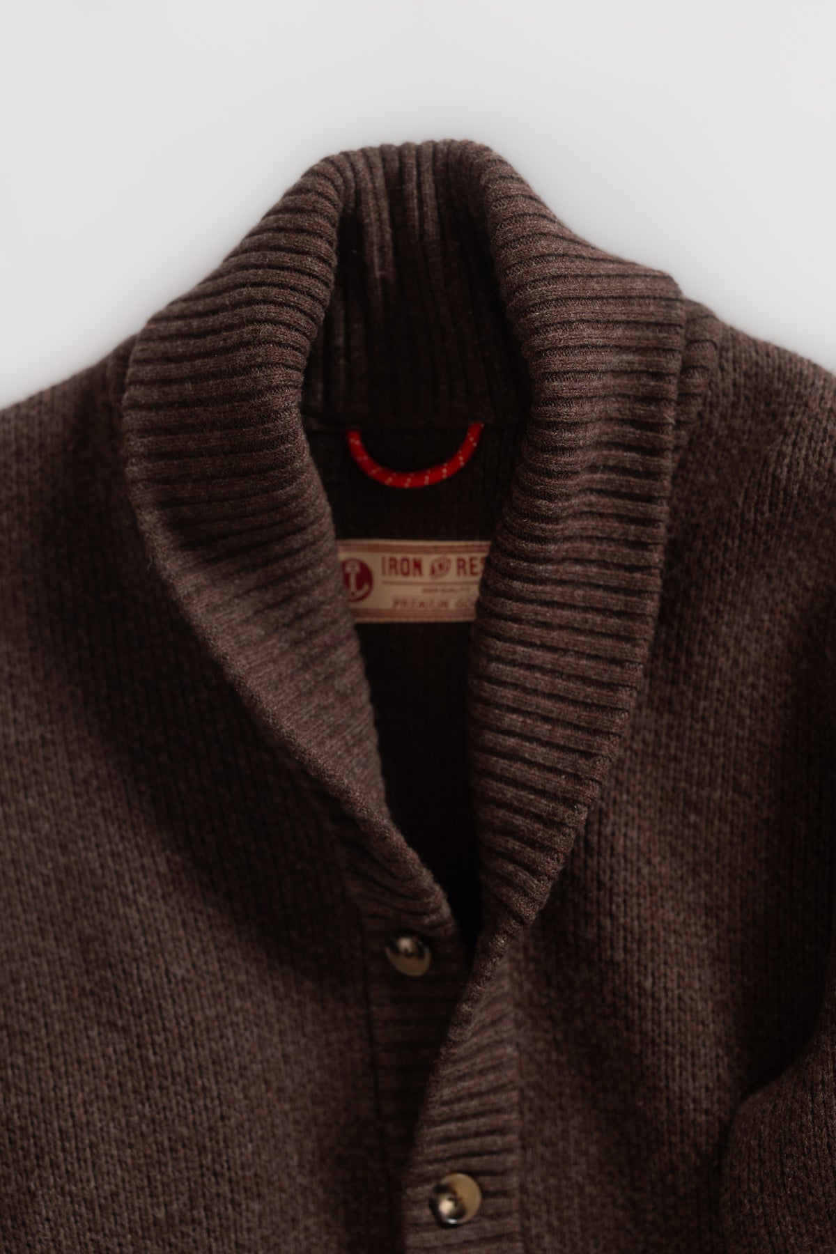 Close-up of a brown ribbed cardigan with a shawl collar and buttons, featuring an Iron and Resin label inside.